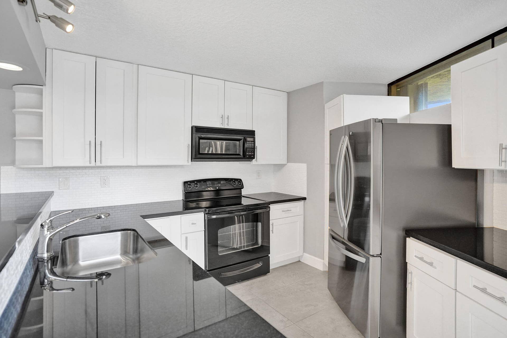 White cabinetry, black countertops, stainless steel refrigerator and tile backsplash