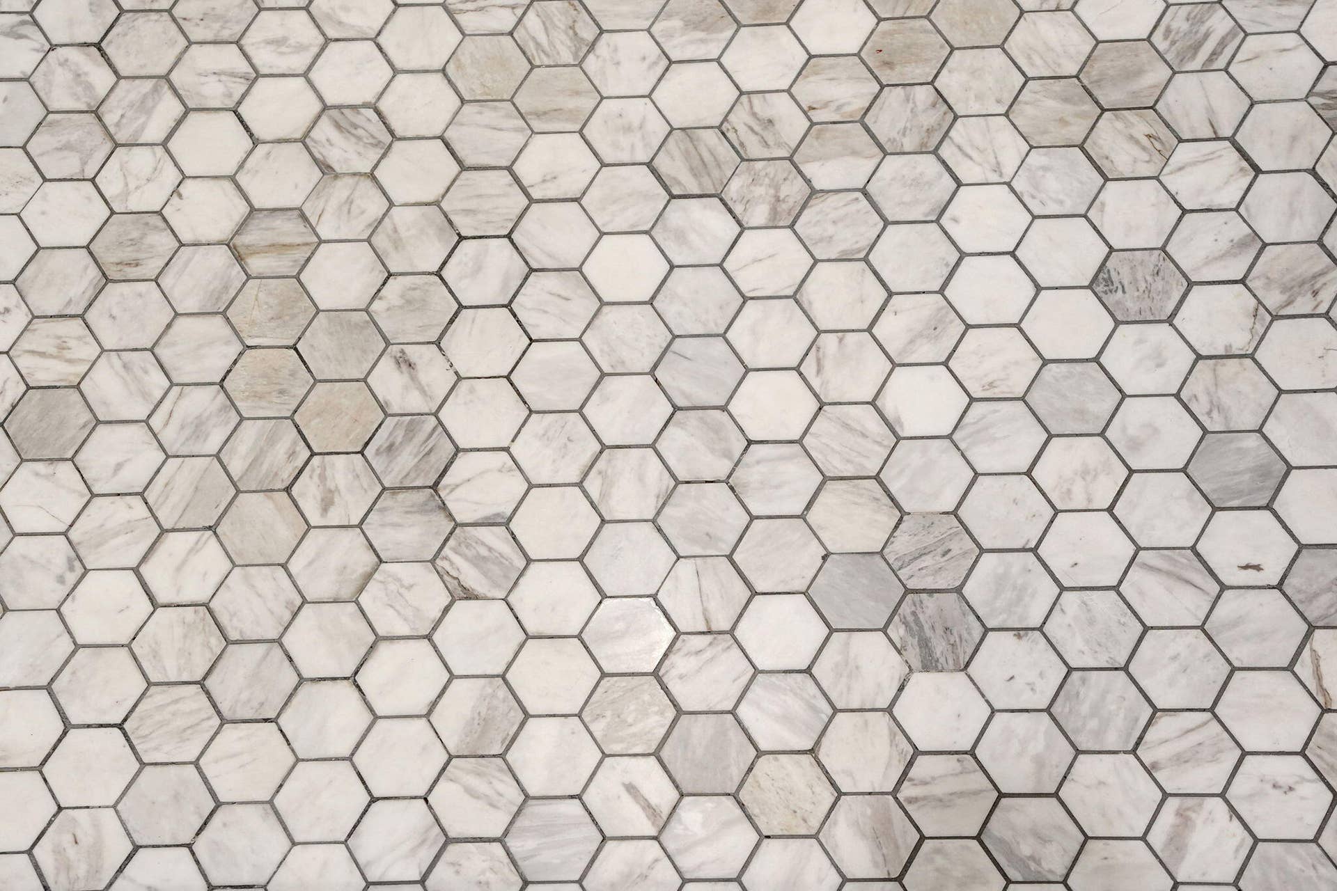 Hexagonal tile flooring featuring varied light-toned stone finishes and contrasting grout