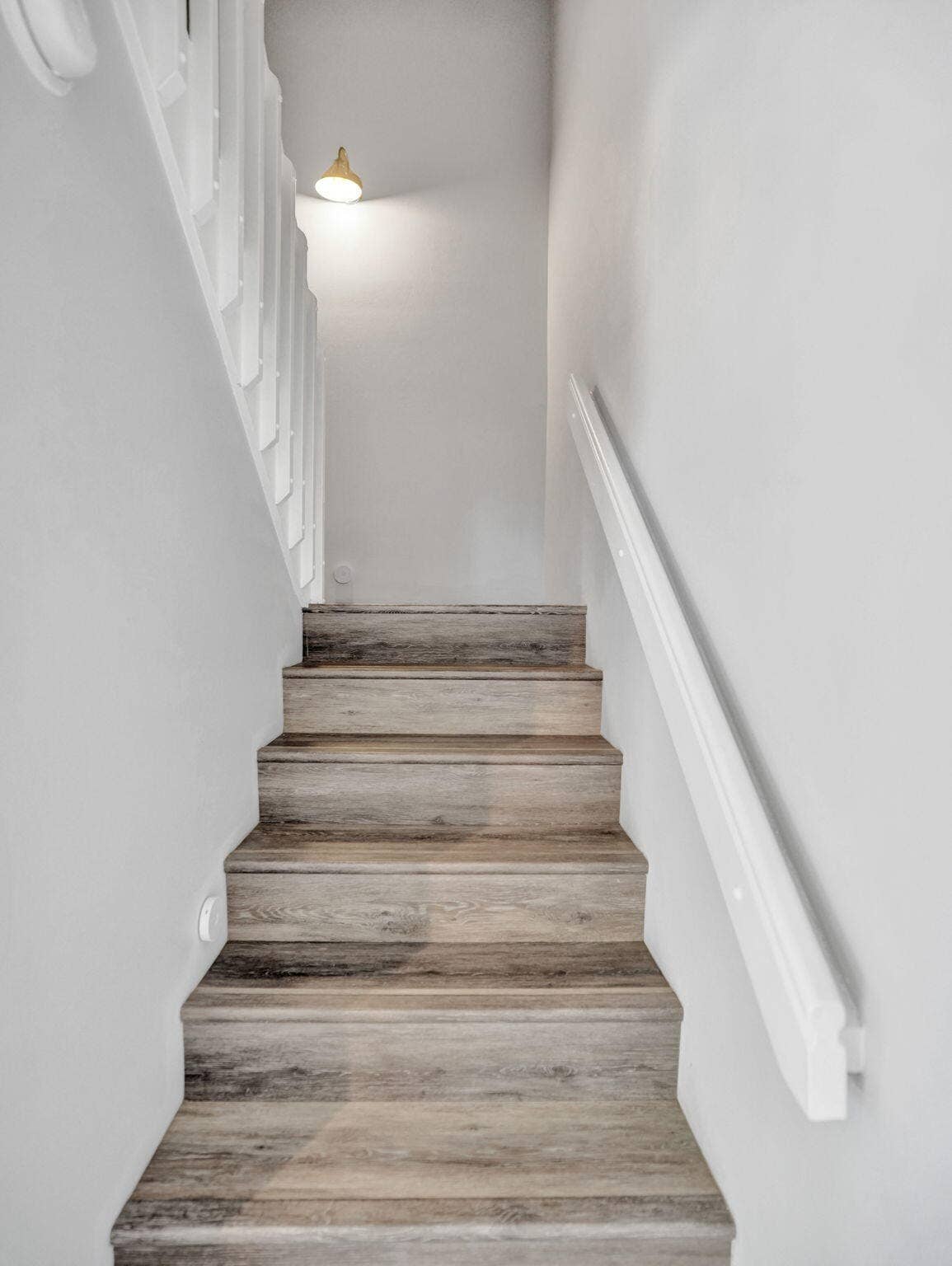 Staircase featuring wood-finish treads, a white handrail, and a decorative wall sconce