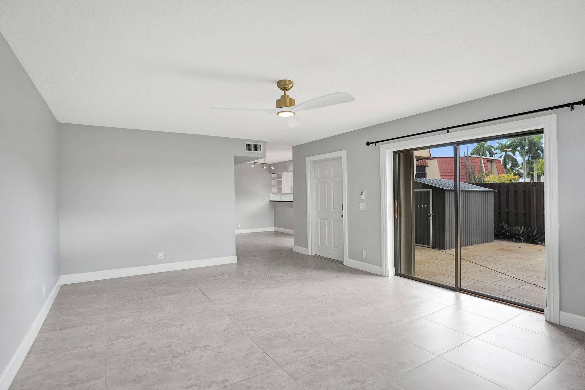 Spacious living room with large format tile flooring, a contemporary ceiling fan, and a sliding glass door leading to an outdoor patio with a privacy fence