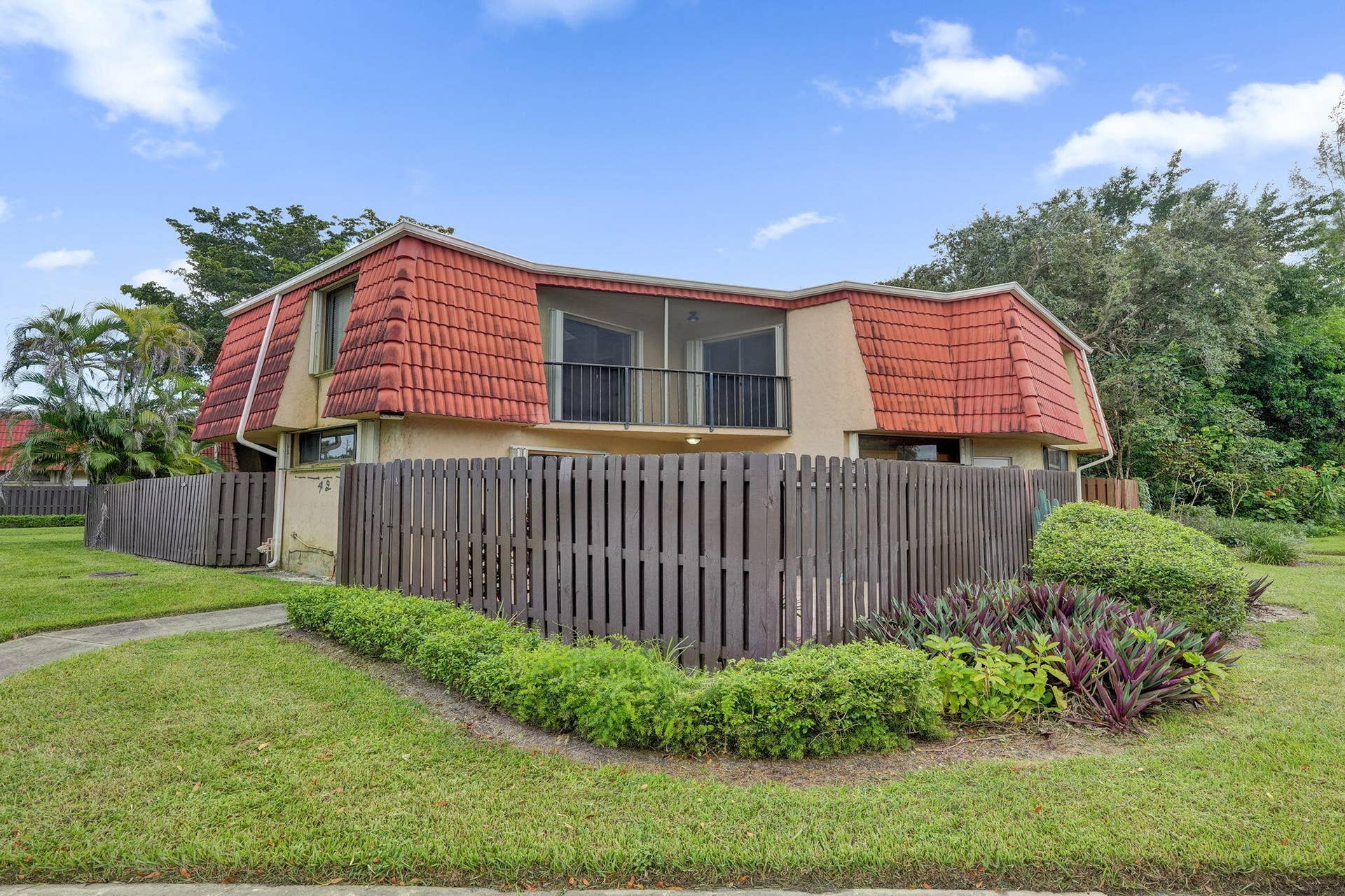 Two-story stucco exterior featuring a red tile roof, an upper-level screened balcony with black railings, and a privacy fence