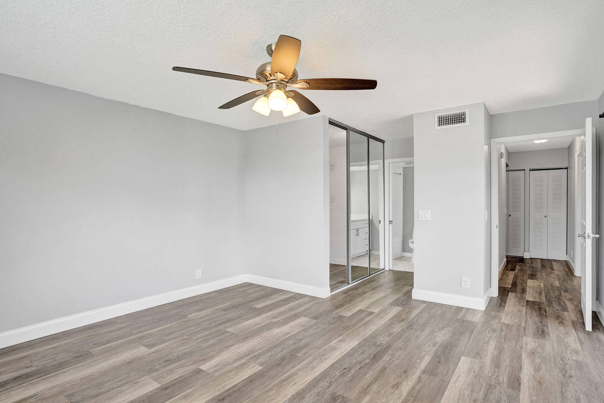 Wood-finish flooring throughout, ceiling fan with integrated lighting, mirrored sliding closet doors, and white paneled interior doors