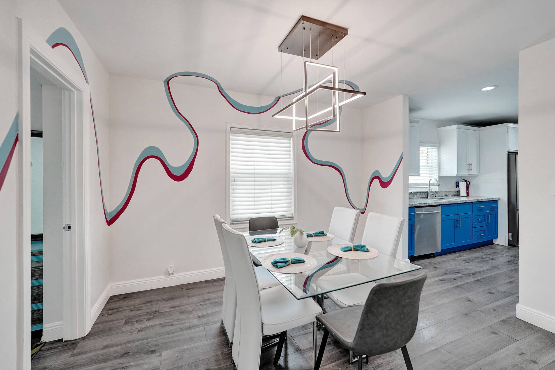 Dining area with wood-finish flooring, a contemporary linear chandelier, and a large window with blinds