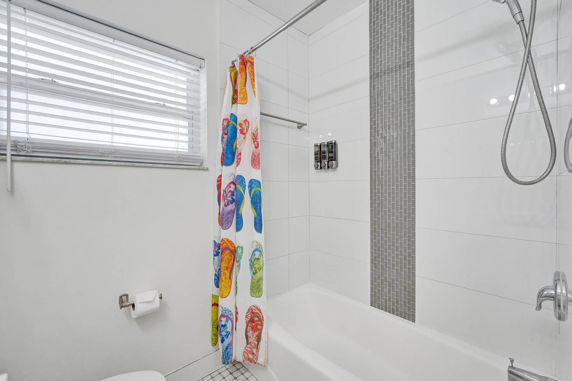 Bathtub with subway tile surround, mosaic accent tile, and a window featuring horizontal blinds