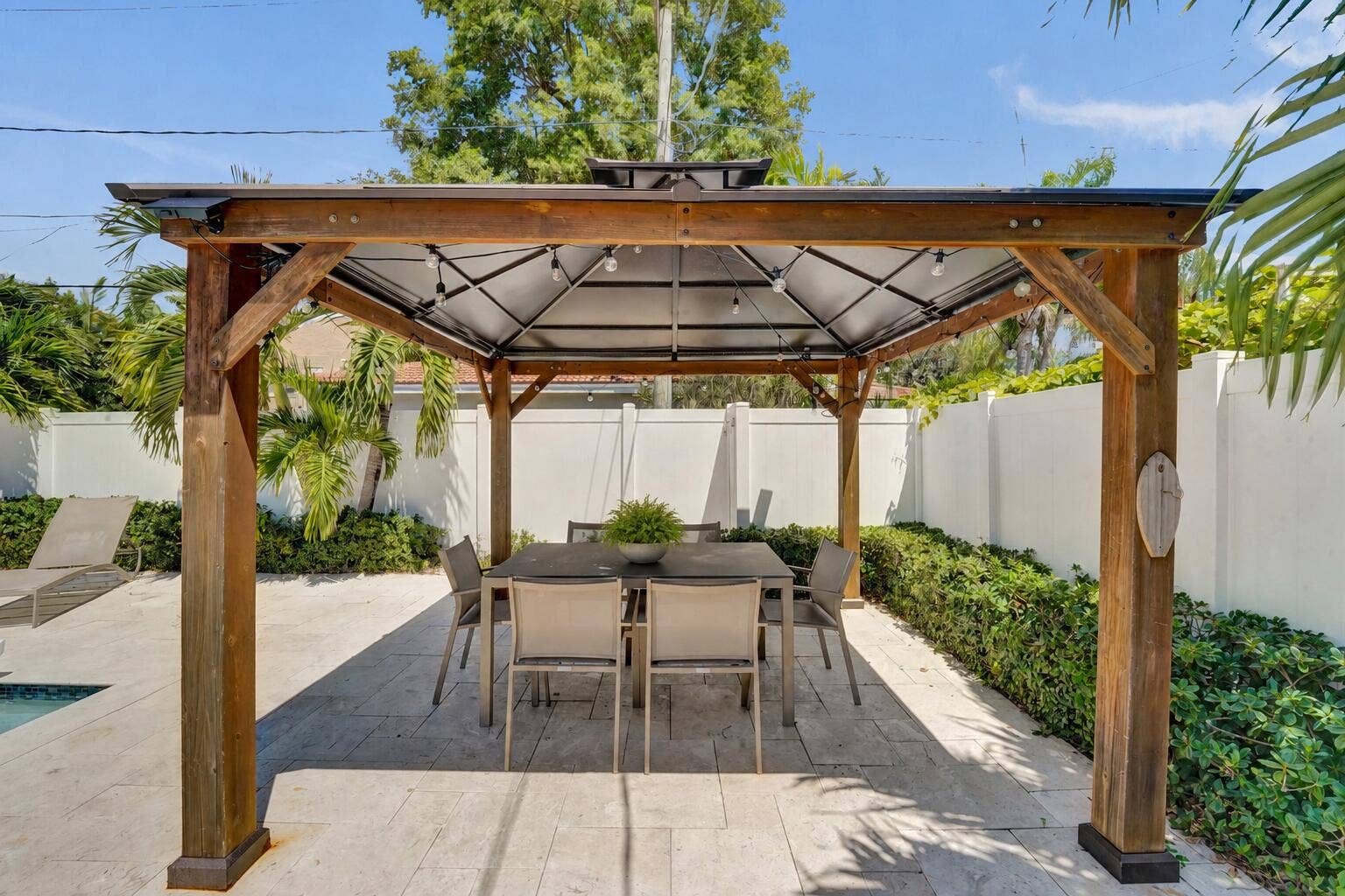 Outdoor living area featuring a wood-frame gazebo with a canopy, string lighting, and a dining set