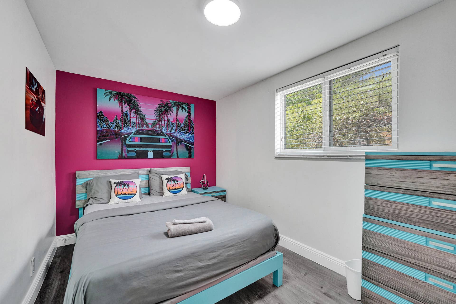 Bedroom featuring wood-finish flooring, a bright accent wall, and a large window with horizontal blinds