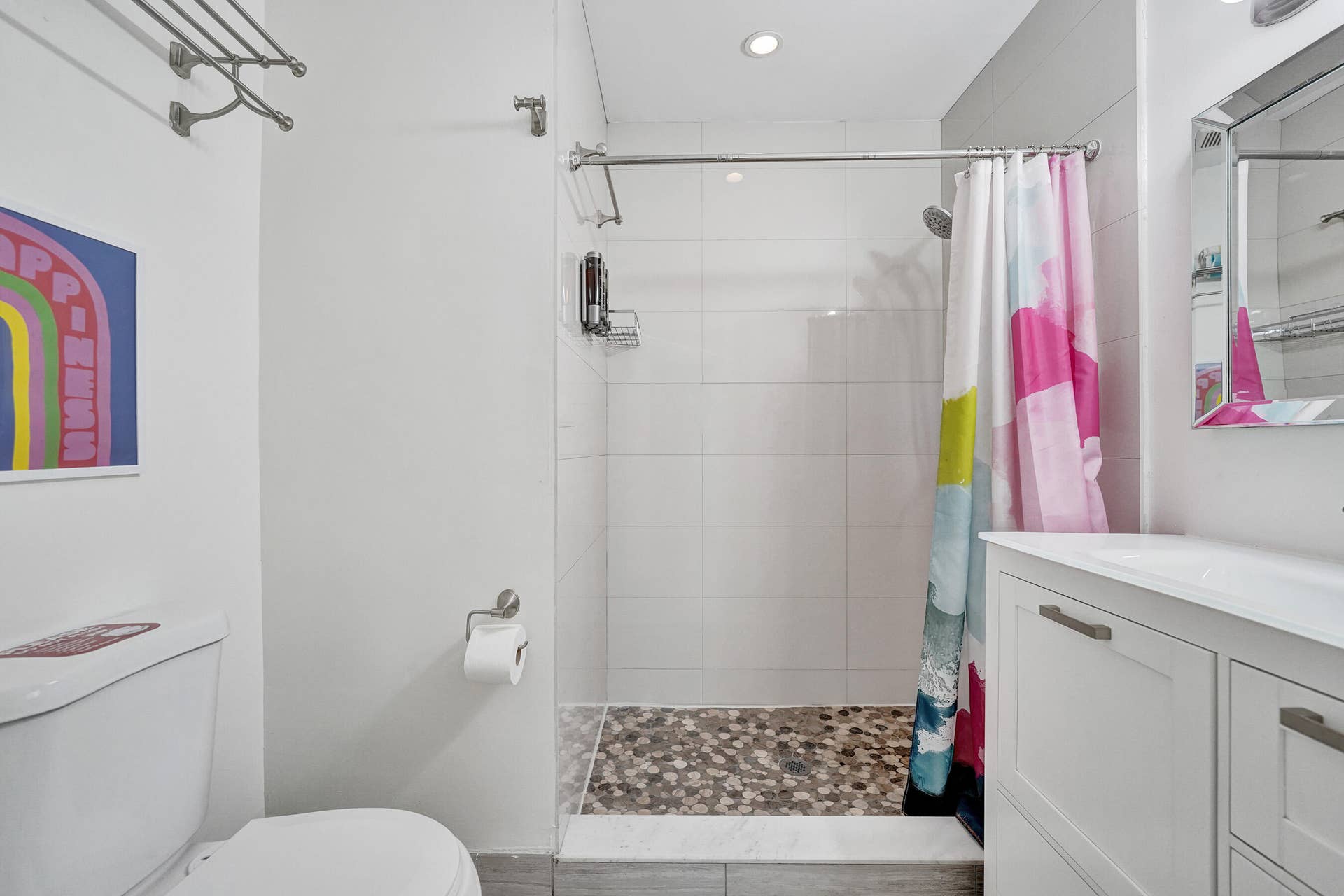 Recessed lighting, glass-enclosed shower, pebble-tiled shower floor, white vanity with integrated sink, and mirrored medicine cabinet