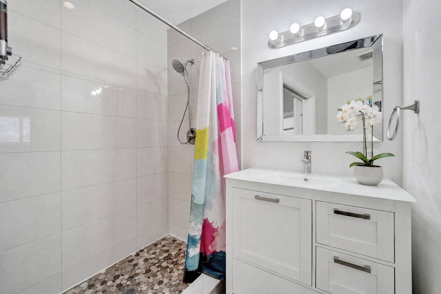 Modern bathroom featuring a clean-lined white vanity with dual drawers and an integrated sink, a large framed mirror with integrated lighting, polished chrome fixtures, and white subway tile walls