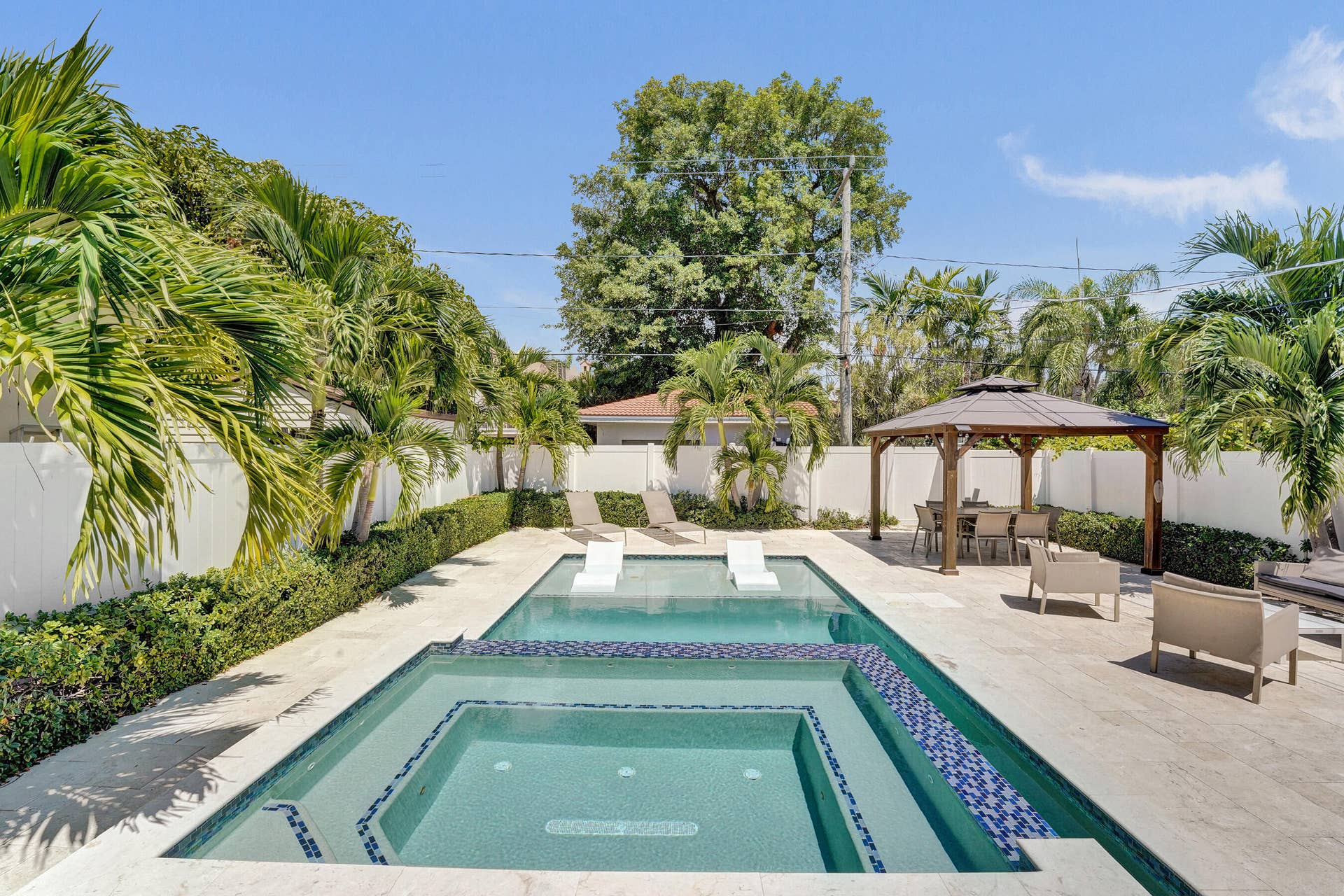 Expansive outdoor area featuring a swimming pool, integrated spa, surrounding paved patio, and a dedicated shaded dining structure