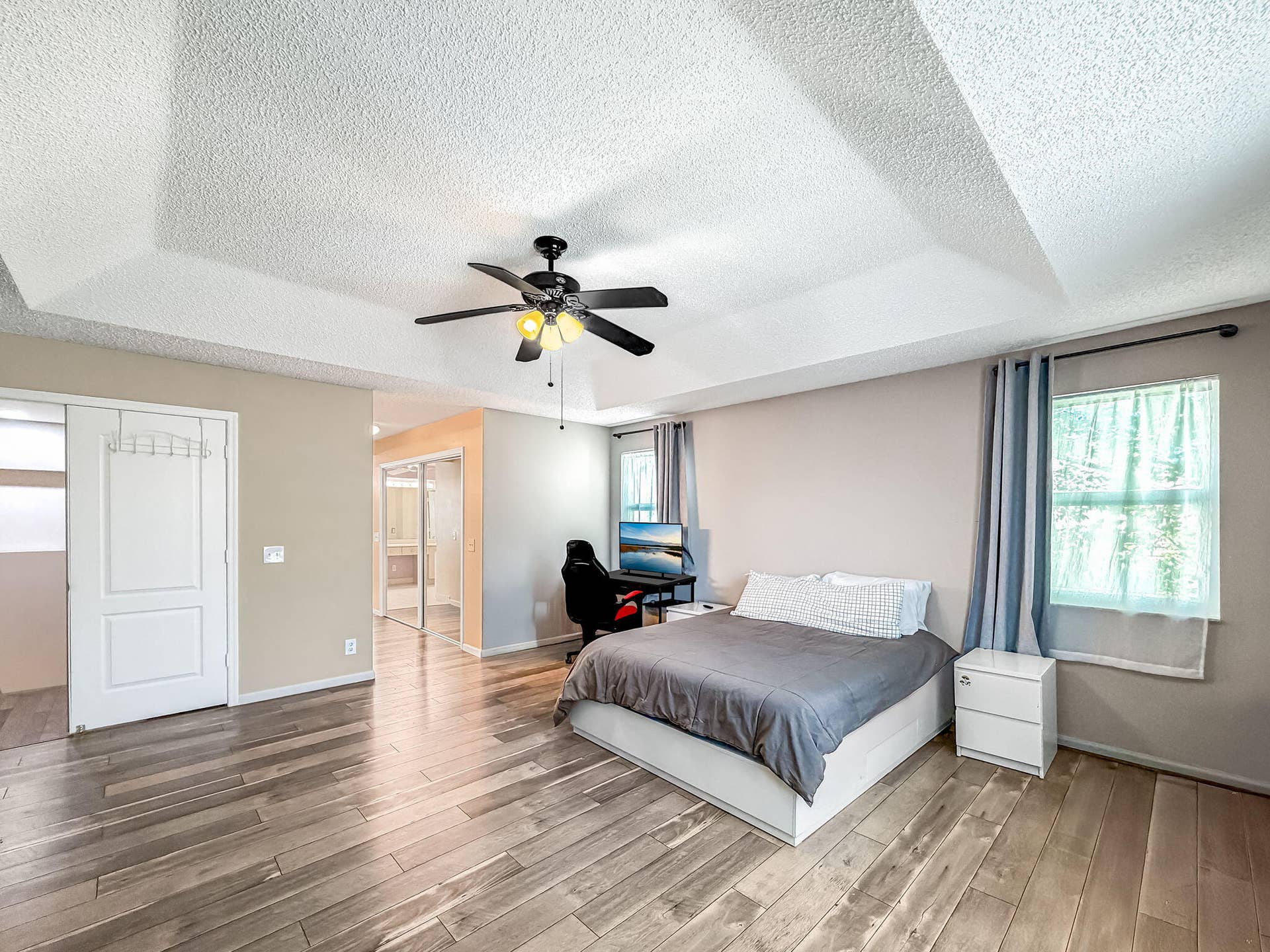 18980 CONCERTO Drive, Boca Raton, FL 33498 Tray ceiling with textured finish, wood-finish flooring, ceiling fan with integrated lighting, and multiple windows with curtain rods