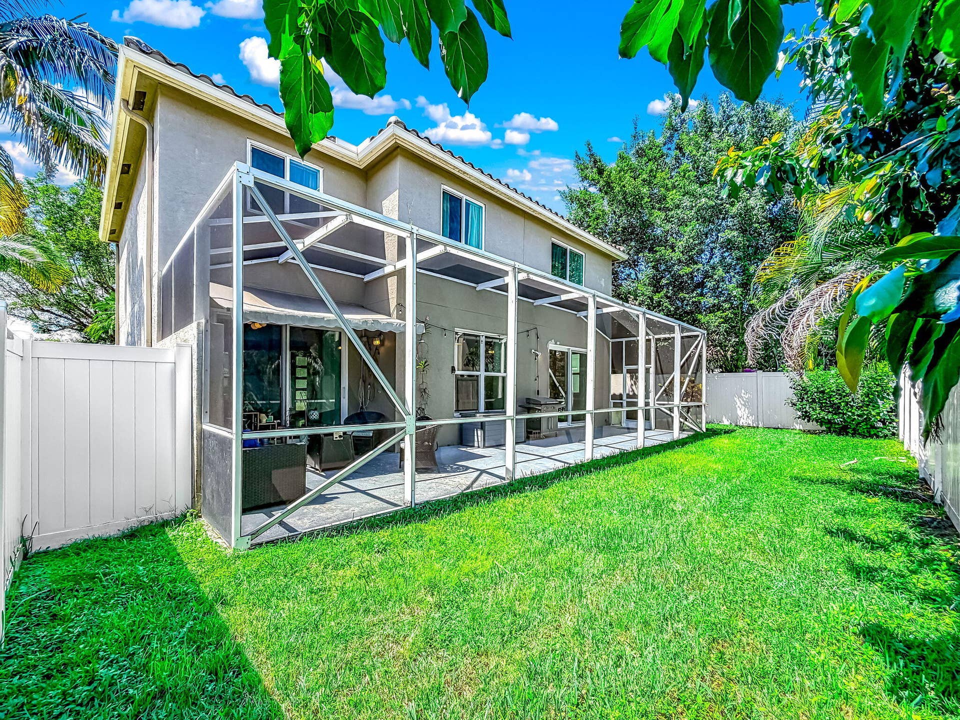18980 CONCERTO Drive, Boca Raton, FL 33498 Expansive grass lawn with a screened patio, white privacy fencing, and mature trees