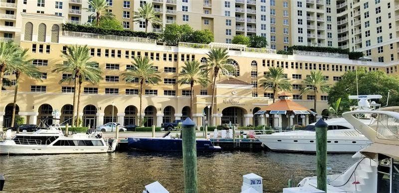 Waterfront building featuring arched entryways, exterior balconies, and lush palm trees