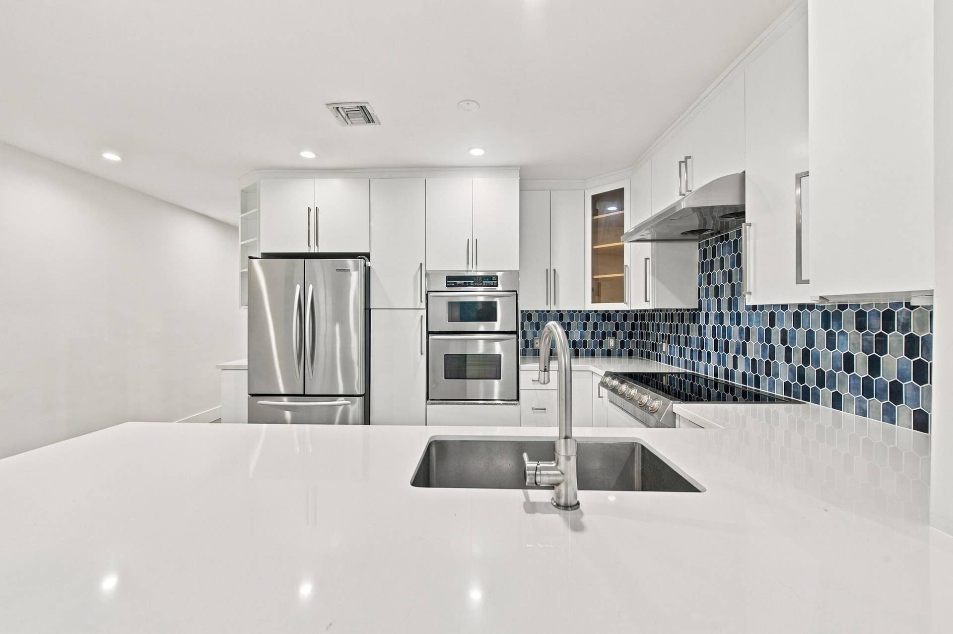 Kitchen featuring a large island with an undermount sink, stainless steel appliances, white cabinetry, and a patterned tile backsplash