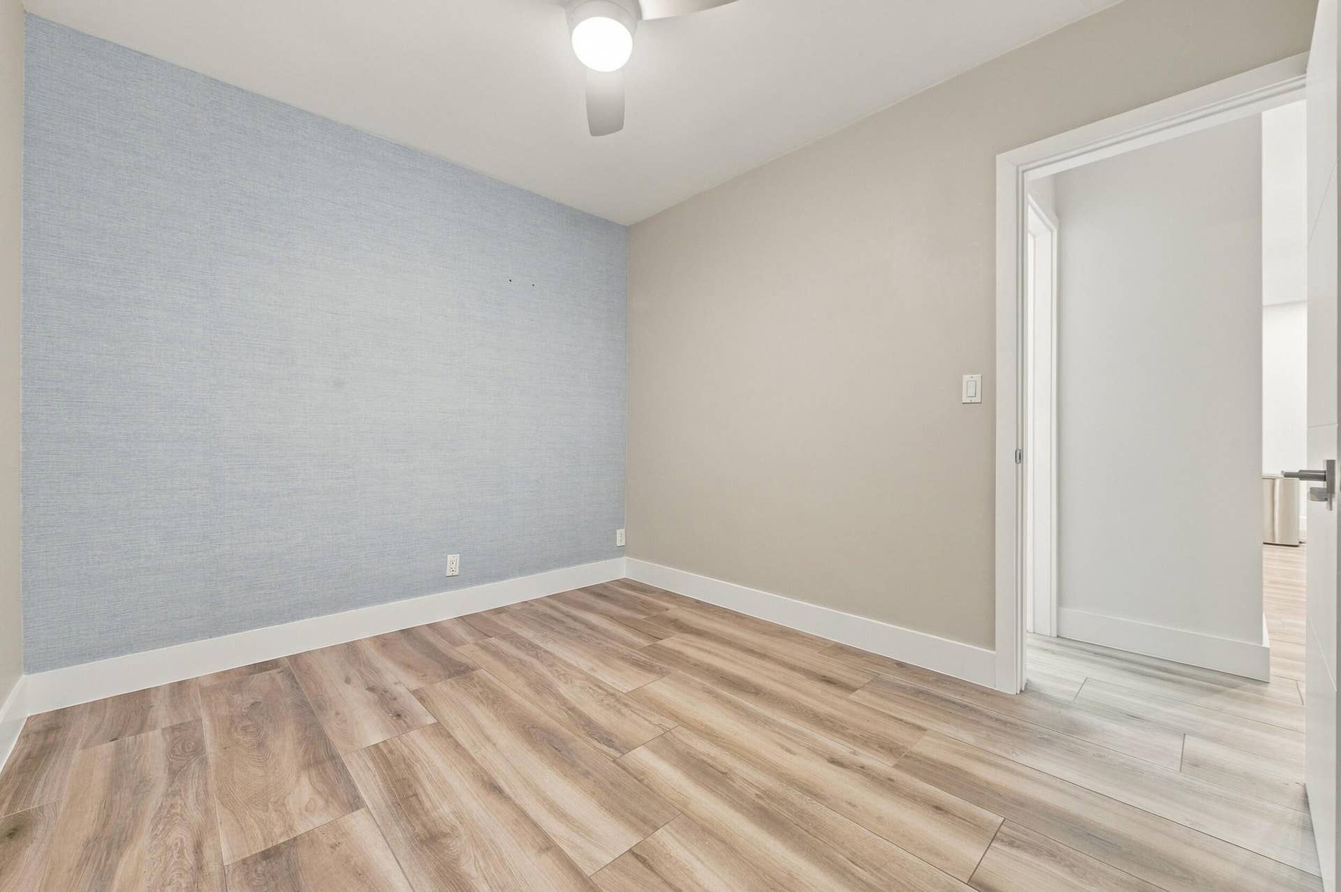 Wood-finish flooring, accent wall with textured wallcovering, ceiling fan, and white trim throughout