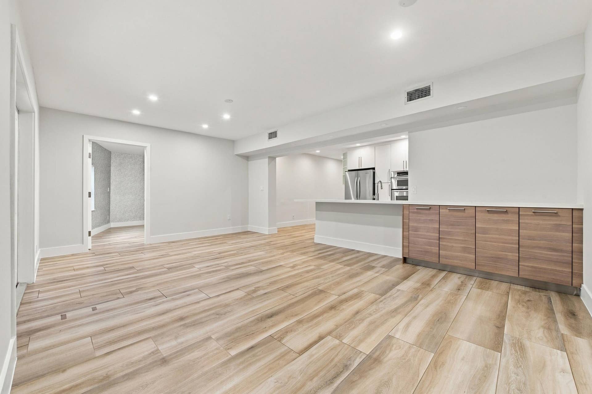 Contemporary kitchen with stainless steel appliances, white cabinetry, and wood-finish flooring
