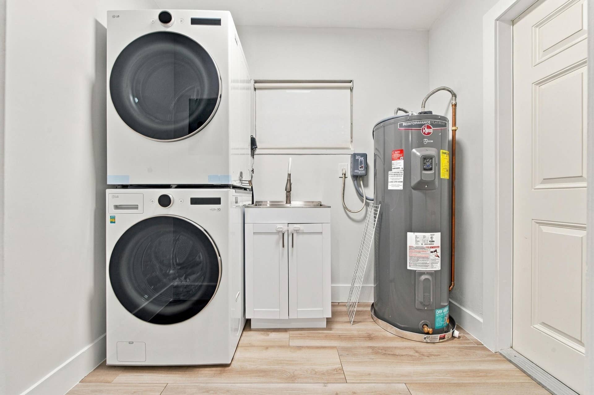 Dedicated laundry area featuring a stacked washer and dryer, utility sink with white cabinetry, and wood-finish flooring