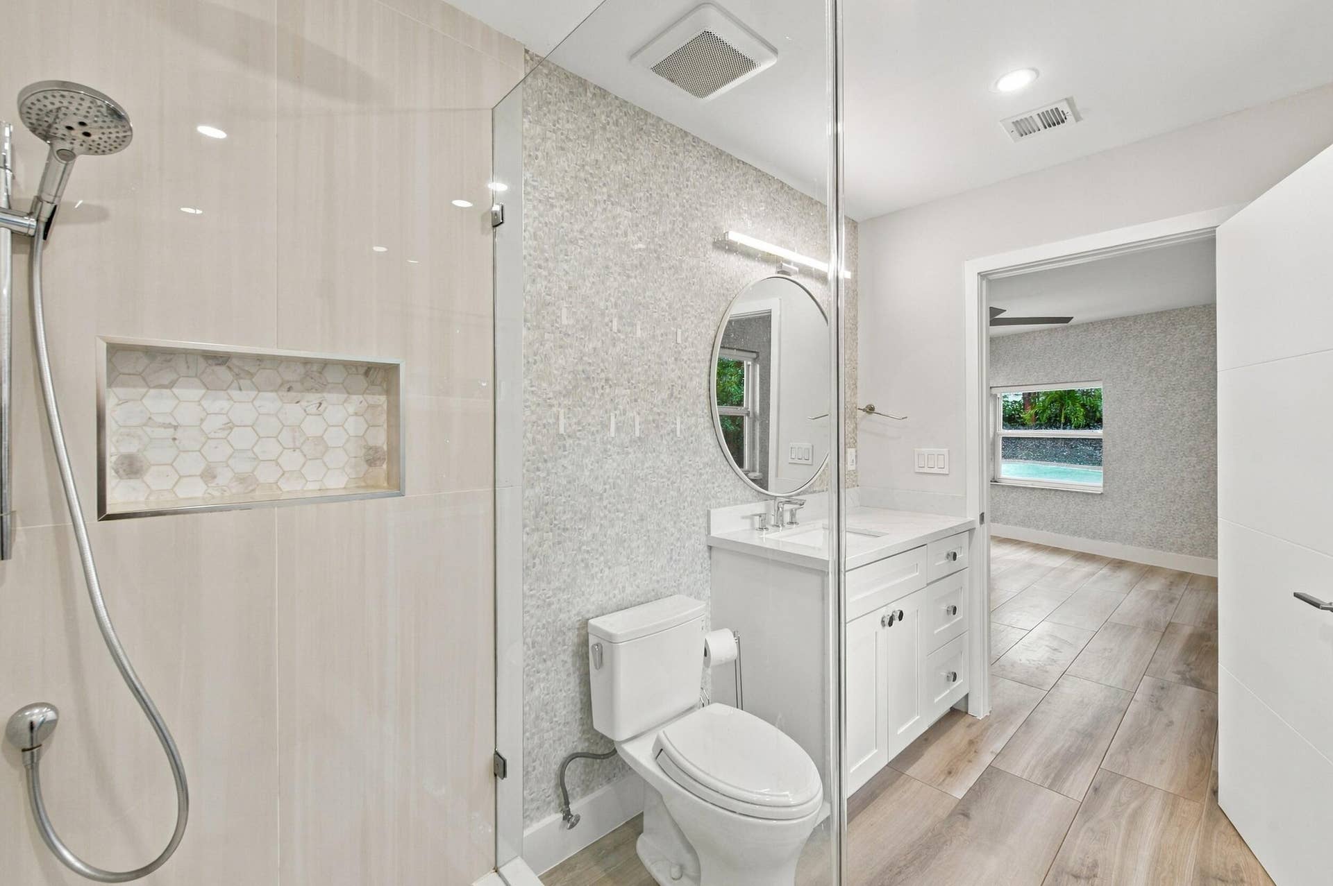 Glass-enclosed shower with a recessed niche, wood-finish flooring, a contemporary vanity with an oval mirror, and recessed lighting