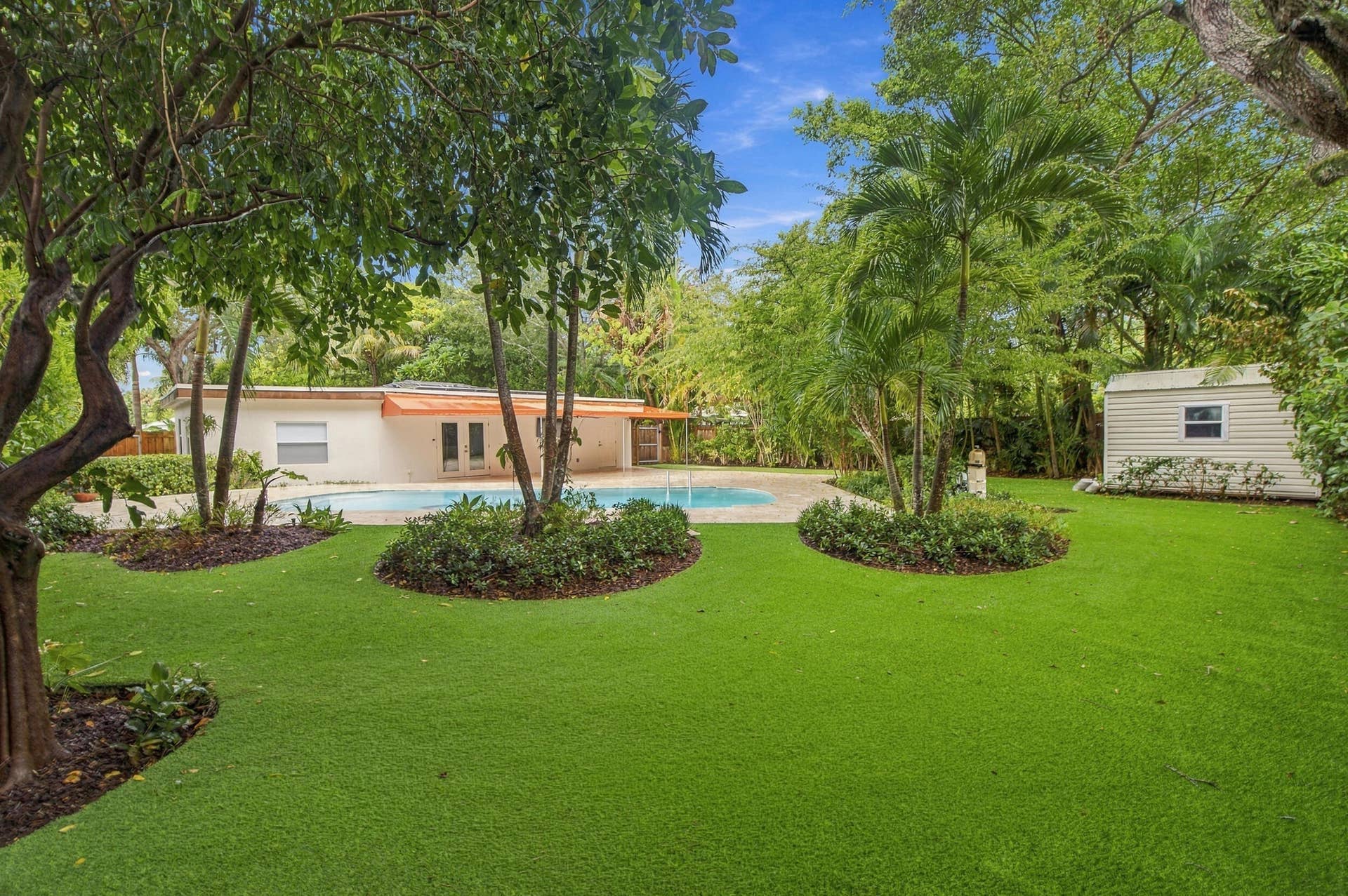 Expansive artificial turf lawn with sculpted garden beds and mature trees