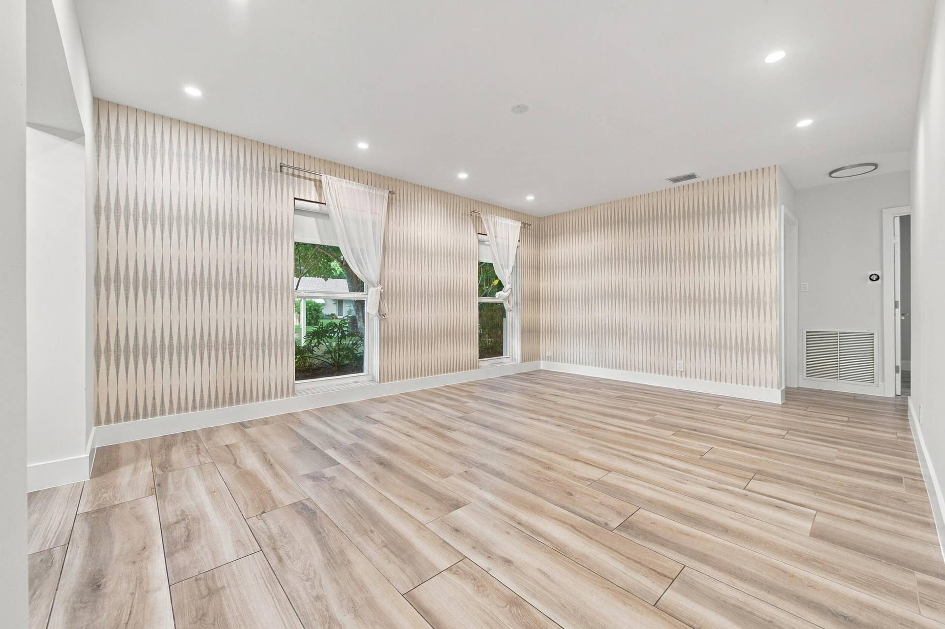 Light wood-finish flooring, recessed ceiling lighting, patterned accent wall, and two windows