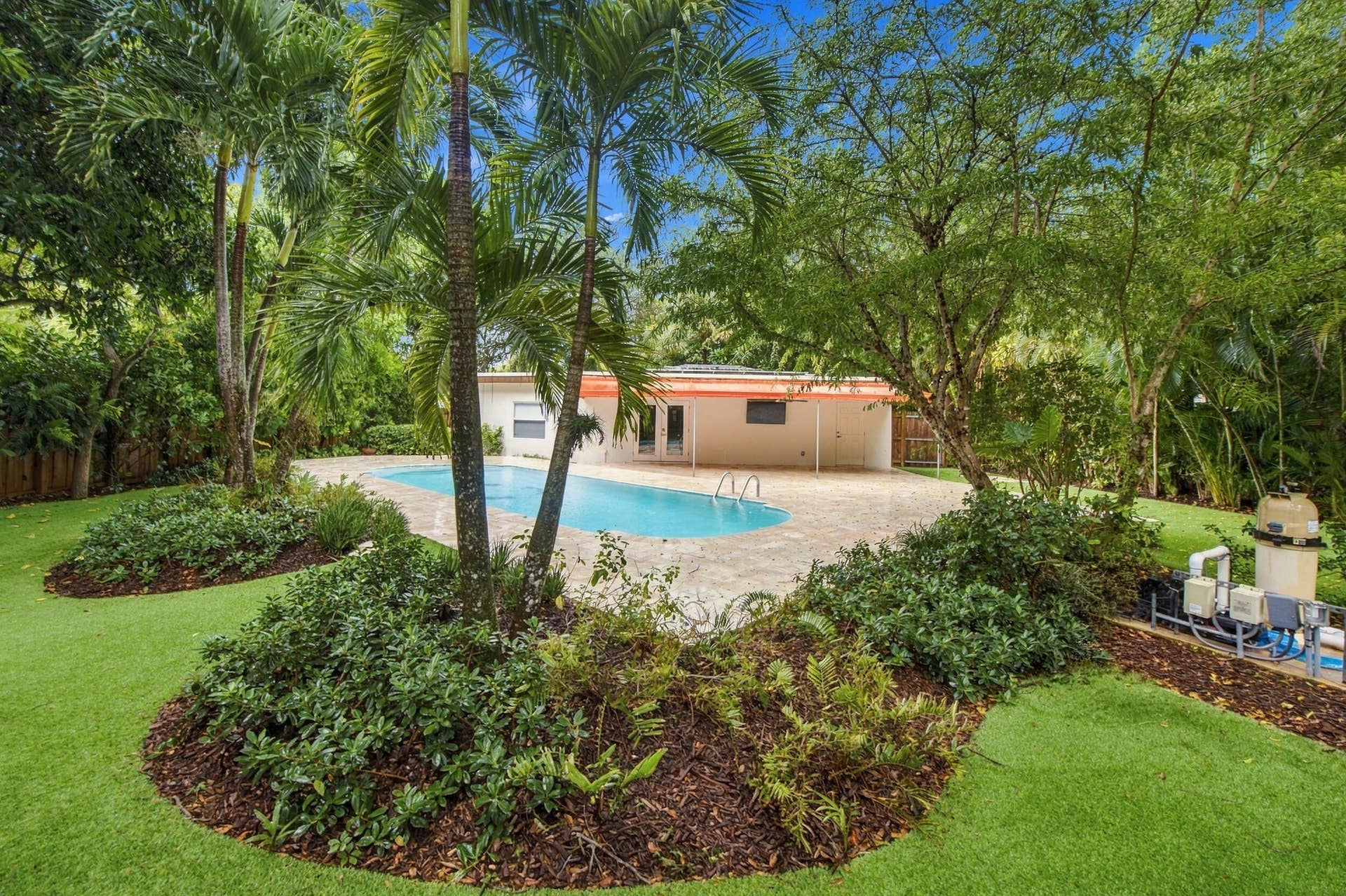 Resort-style backyard featuring a freeform swimming pool, extensive pool decking, and lush tropical landscaping