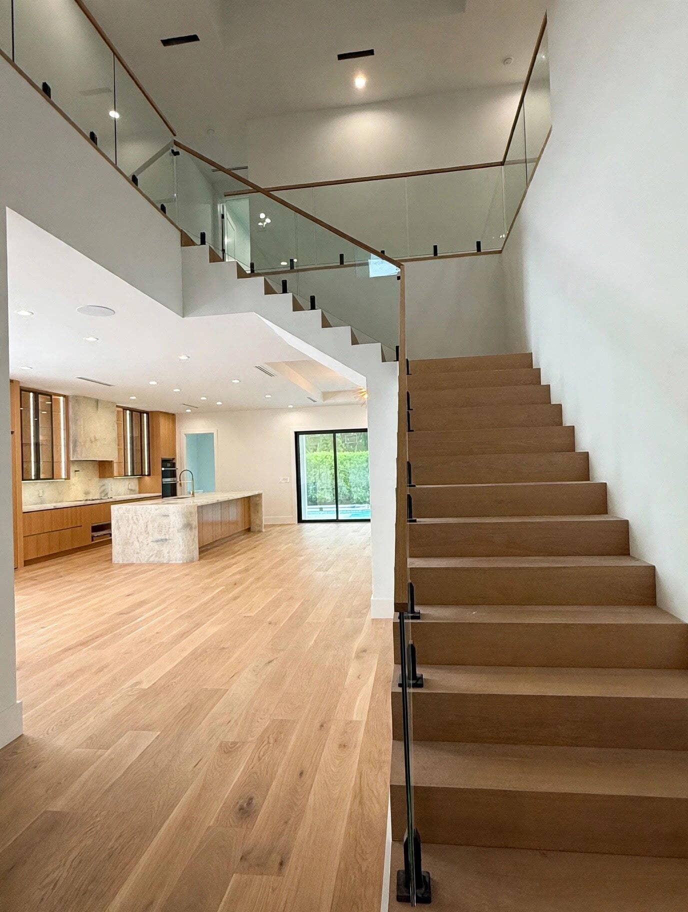 1109 PROSPERITY VILLAGE Drive, North Palm Beach, FL 33410 Floating wood staircase with glass railing and wood handrail, hardwood flooring, recessed lighting, and a kitchen featuring a stone-clad island