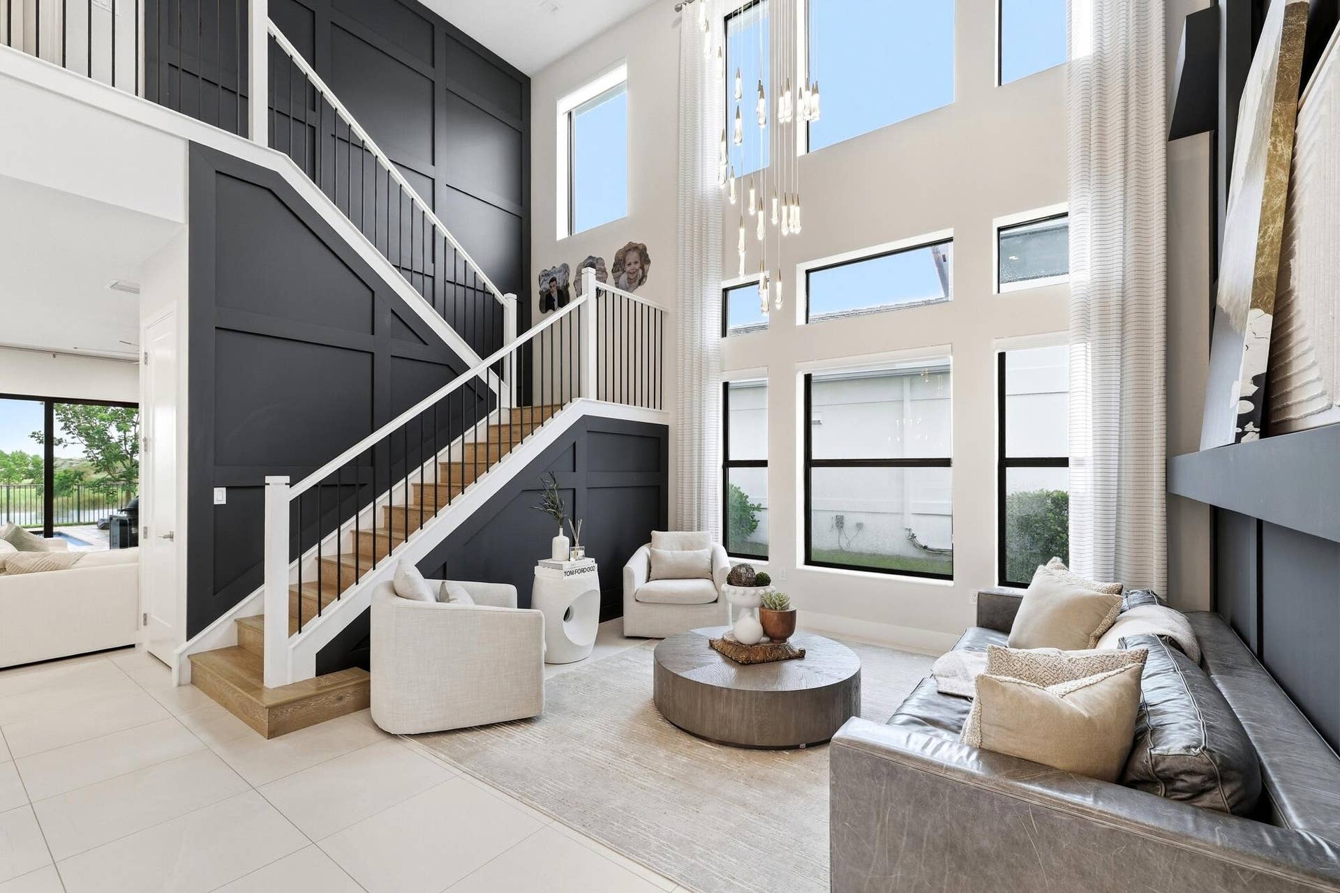 Two-story living area with high ceilings, multiple large windows, a built-in shelving unit, and a prominent staircase with wood-finish treads and an open balustrade