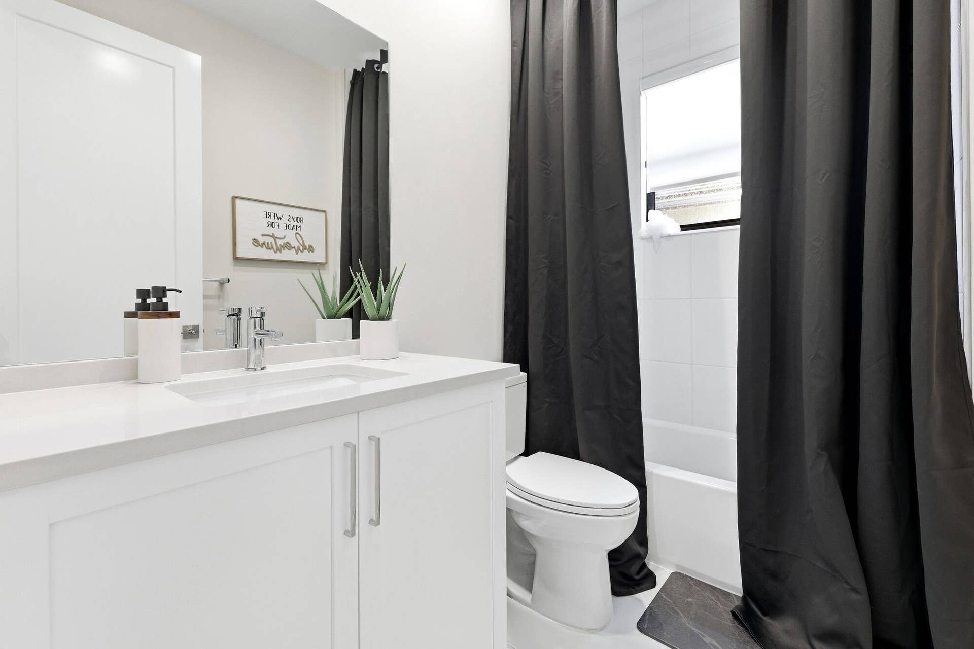 White vanity with integrated sink, chrome faucet, white countertop, white toilet, and white tiled shower surround