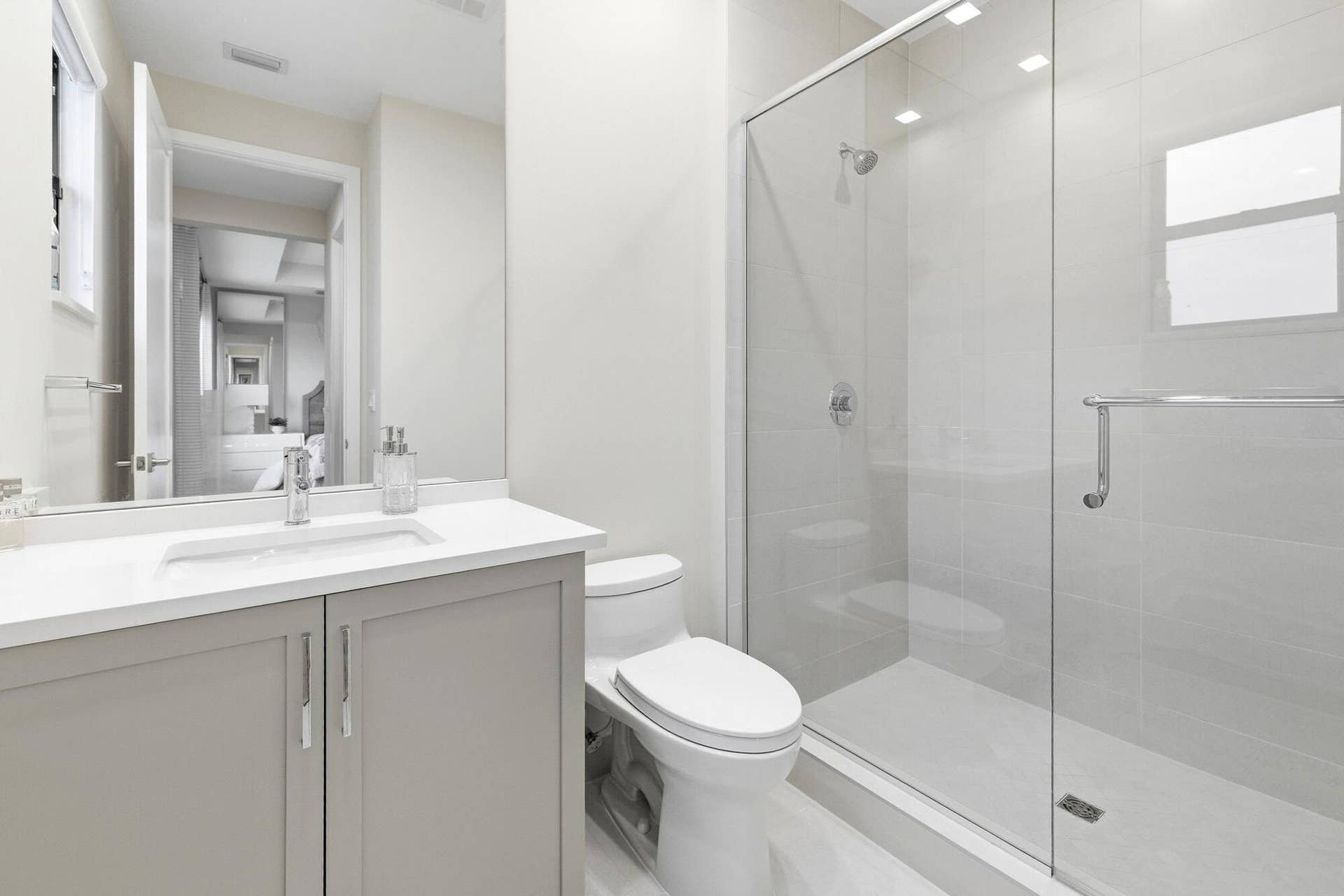 Contemporary bathroom featuring a single vanity with light grey cabinetry, a rectangular undermount sink, and a glass-enclosed shower with a chrome showerhead
