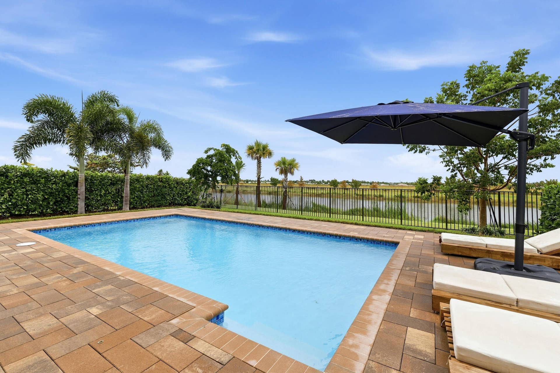 Rectangular swimming pool with paver decking, enclosed by a black metal fence, overlooking a body of water
