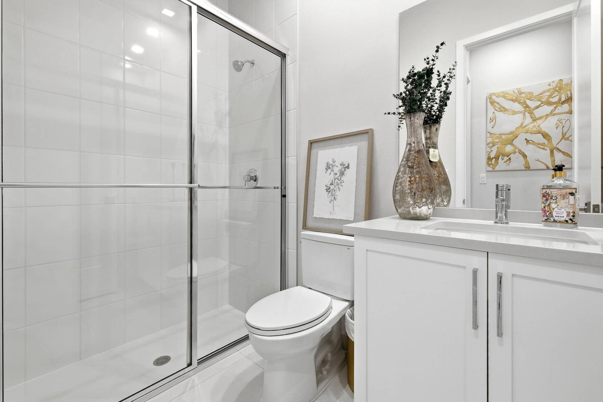 Shower with sliding glass doors, white tiled walls, white vanity with integrated sink, chrome faucet, and white cabinetry