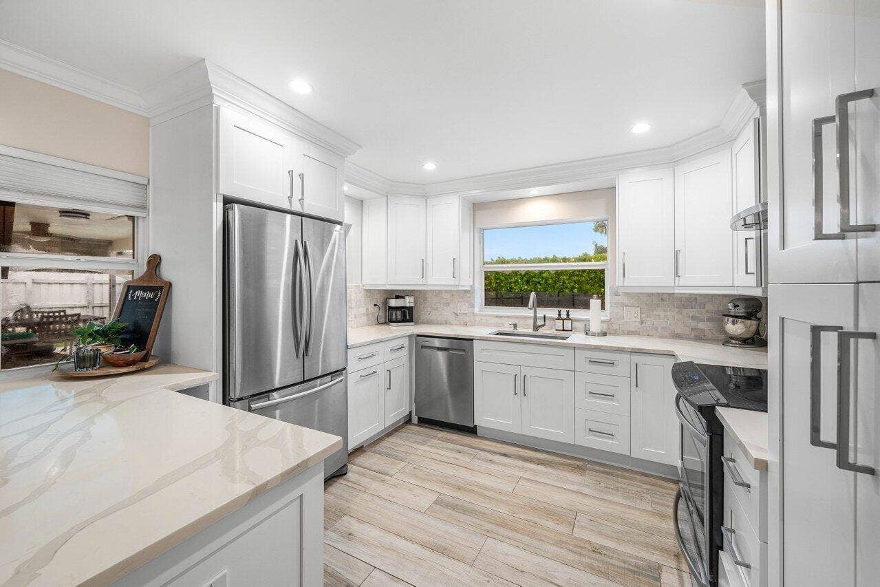 979 SW 13TH Drive, Boca Raton, FL 33486 White cabinetry, stainless steel appliances, and a window above the sink brighten the kitchen.