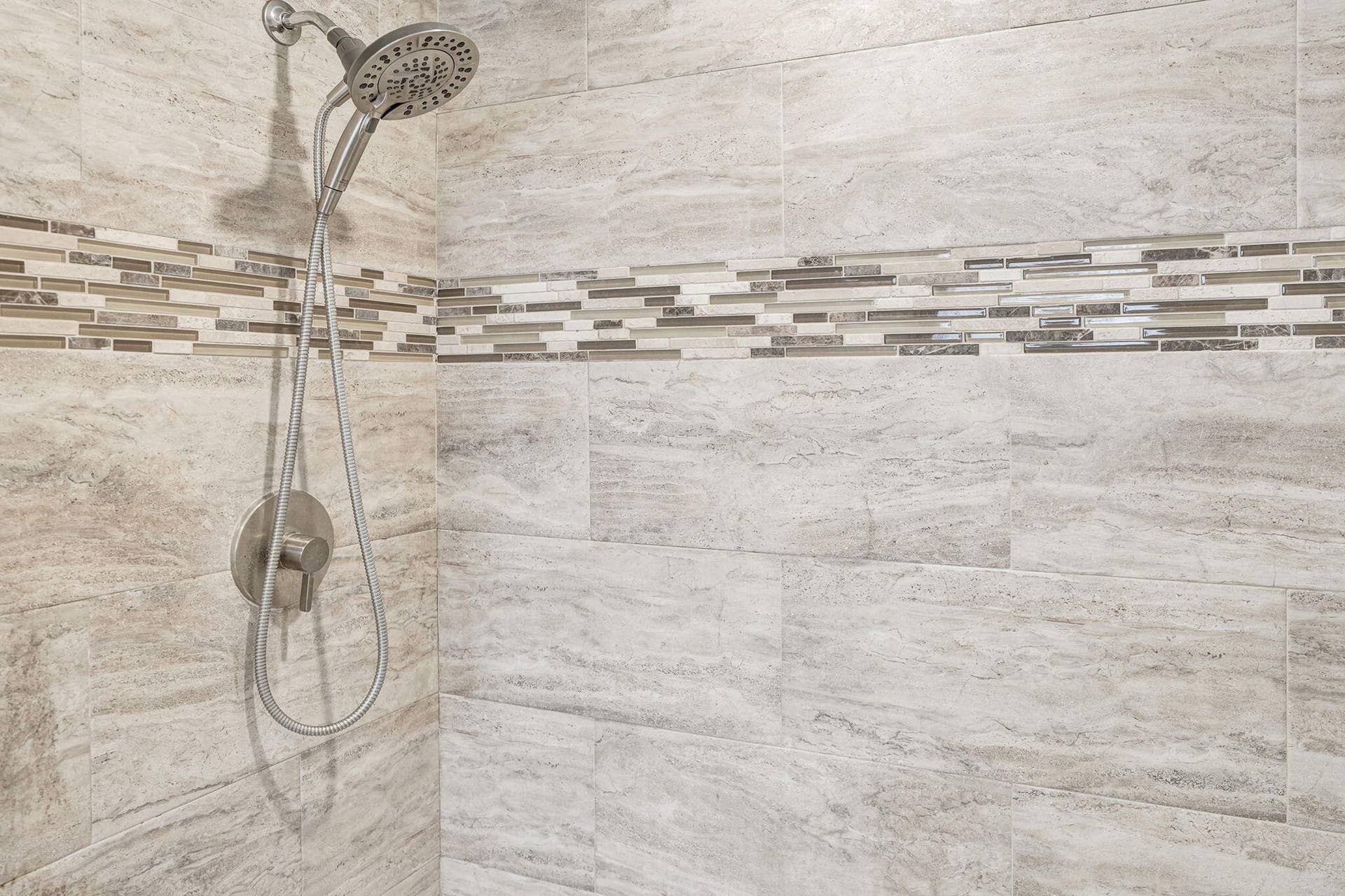 Shower featuring a multi-function shower head, brushed nickel fixtures, and a decorative mosaic tile accent band