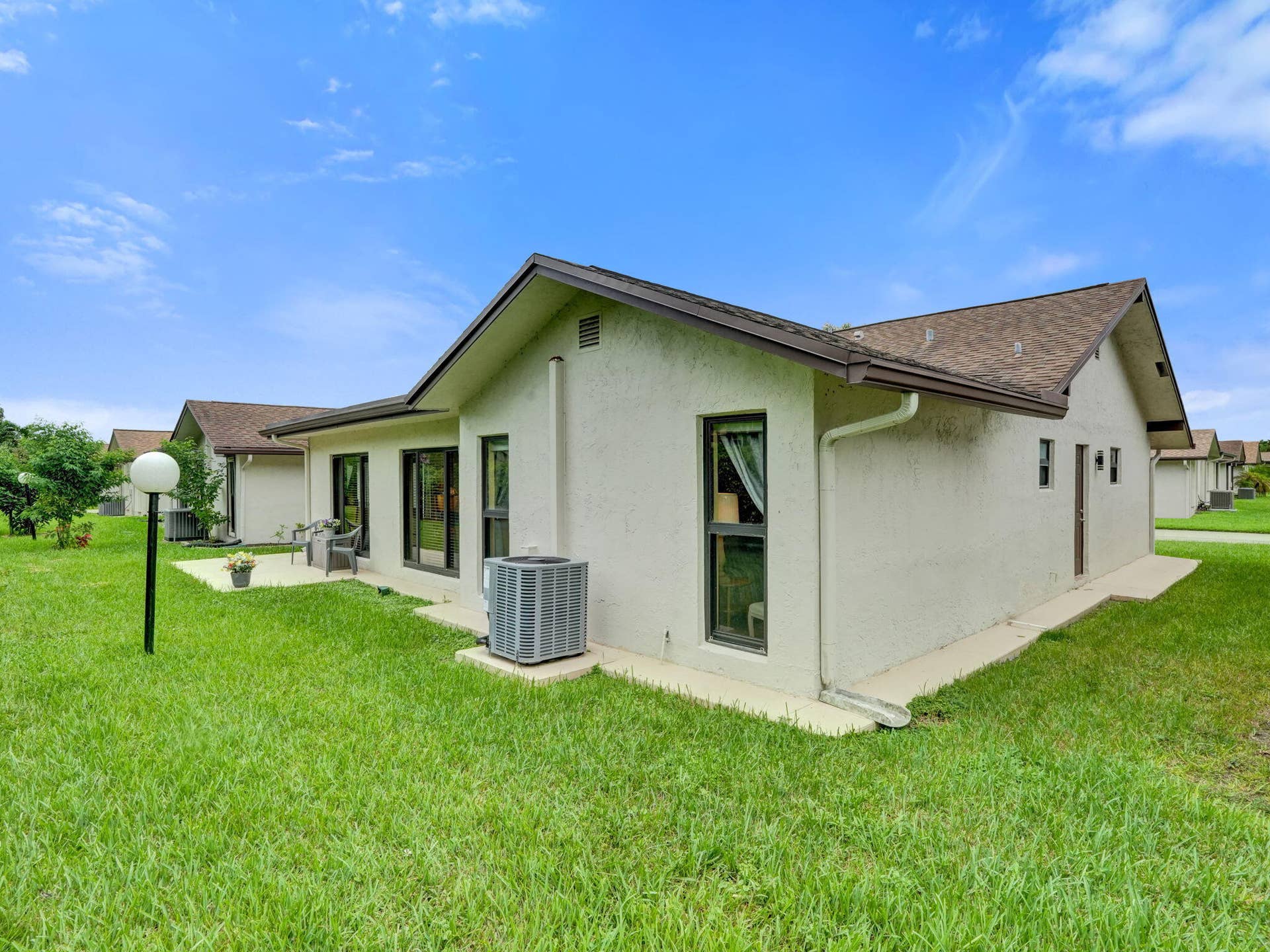 2085 SW 15th Place, Deerfield Beach, FL 33442 Stucco exterior, gabled roof, multiple windows, concrete patio, and a grass lawn