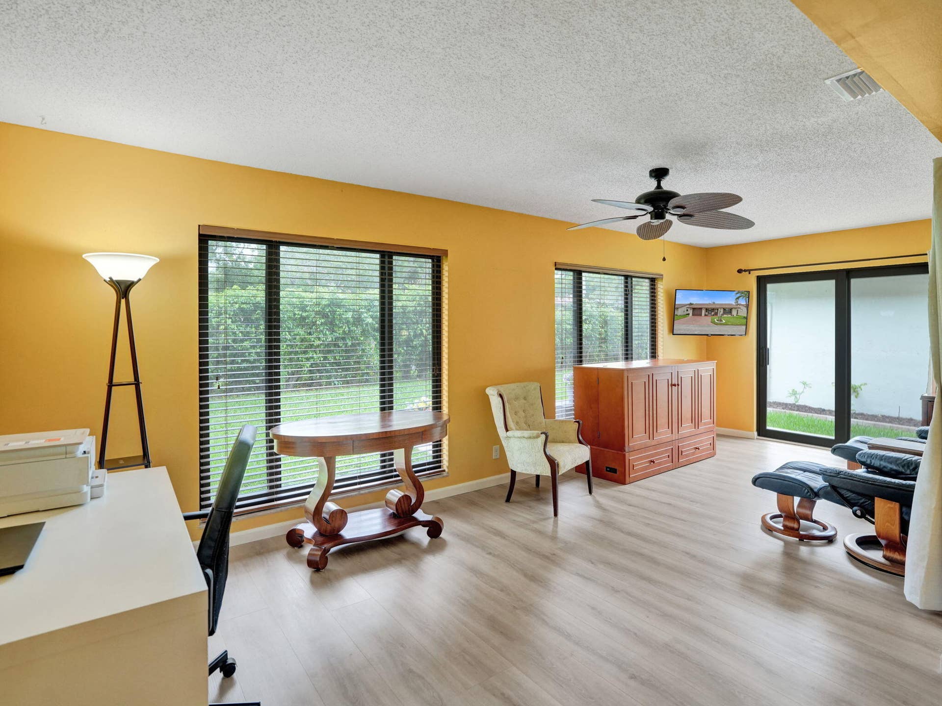 2085 SW 15th Place, Deerfield Beach, FL 33442 Light wood-finish flooring, multiple large windows with horizontal blinds, and a ceiling fan with integrated lighting