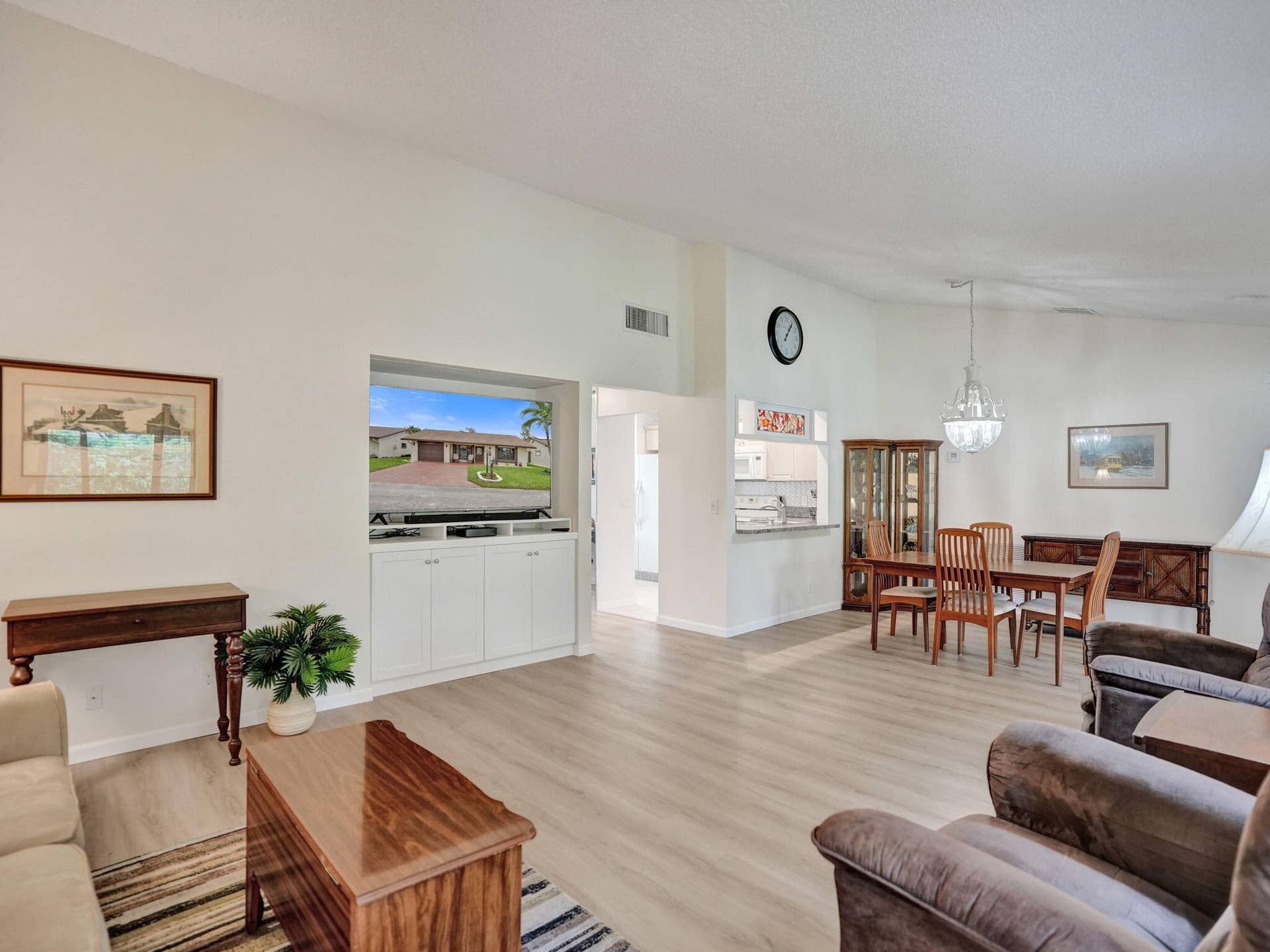 2085 SW 15th Place, Deerfield Beach, FL 33442 Open-concept living space featuring wood-finish flooring, a built-in media cabinet, a dining area with chandelier, and a breakfast bar opening to the kitchen
