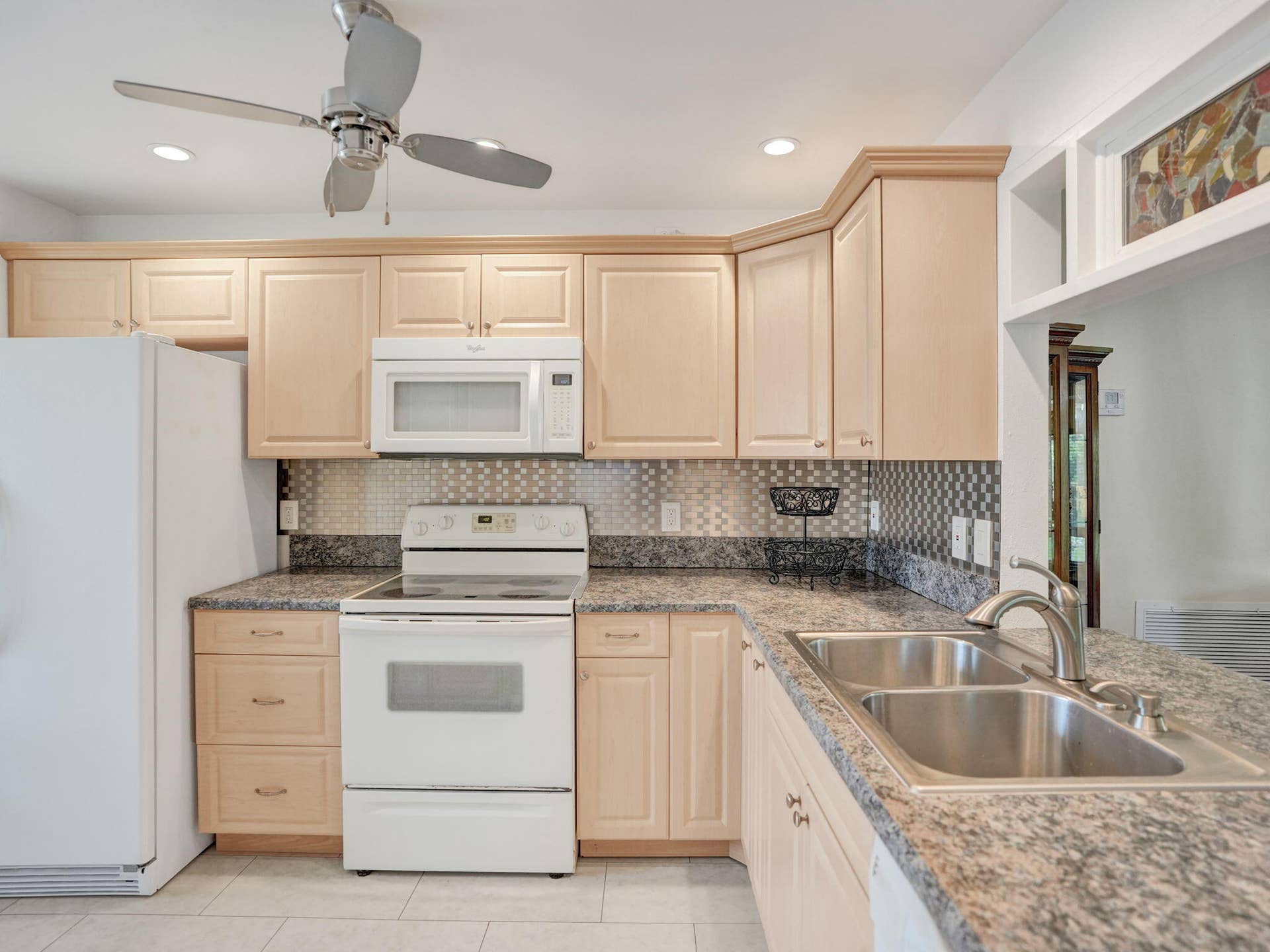 2085 SW 15th Place, Deerfield Beach, FL 33442 Light wood-finish cabinetry with crown molding, granite-patterned countertops, stainless steel double-basin sink with a chrome faucet, and a metallic tile backsplash