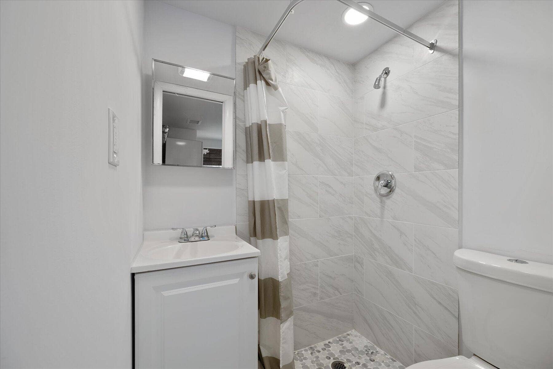 714 W Lakewood Road, #B, West Palm Beach, West Palm Beach, FL 33405 Bathroom featuring a white vanity with integrated sink, chrome faucet, medicine cabinet with integrated lighting, tiled shower surround, and mosaic tile shower floor