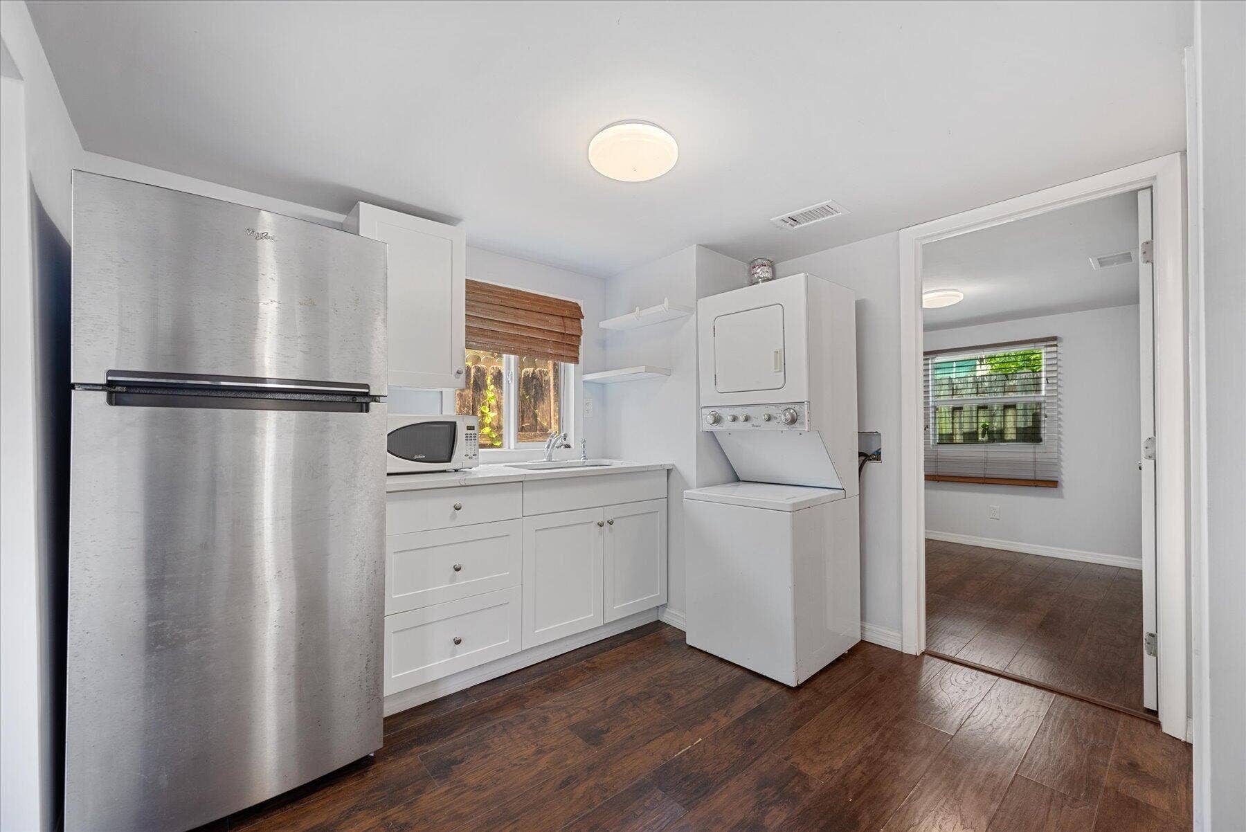 714 W Lakewood Road, #B, West Palm Beach, West Palm Beach, FL 33405 Stainless steel refrigerator, white cabinetry, wood-finish flooring, white countertop, and stacked washer/dryer unit