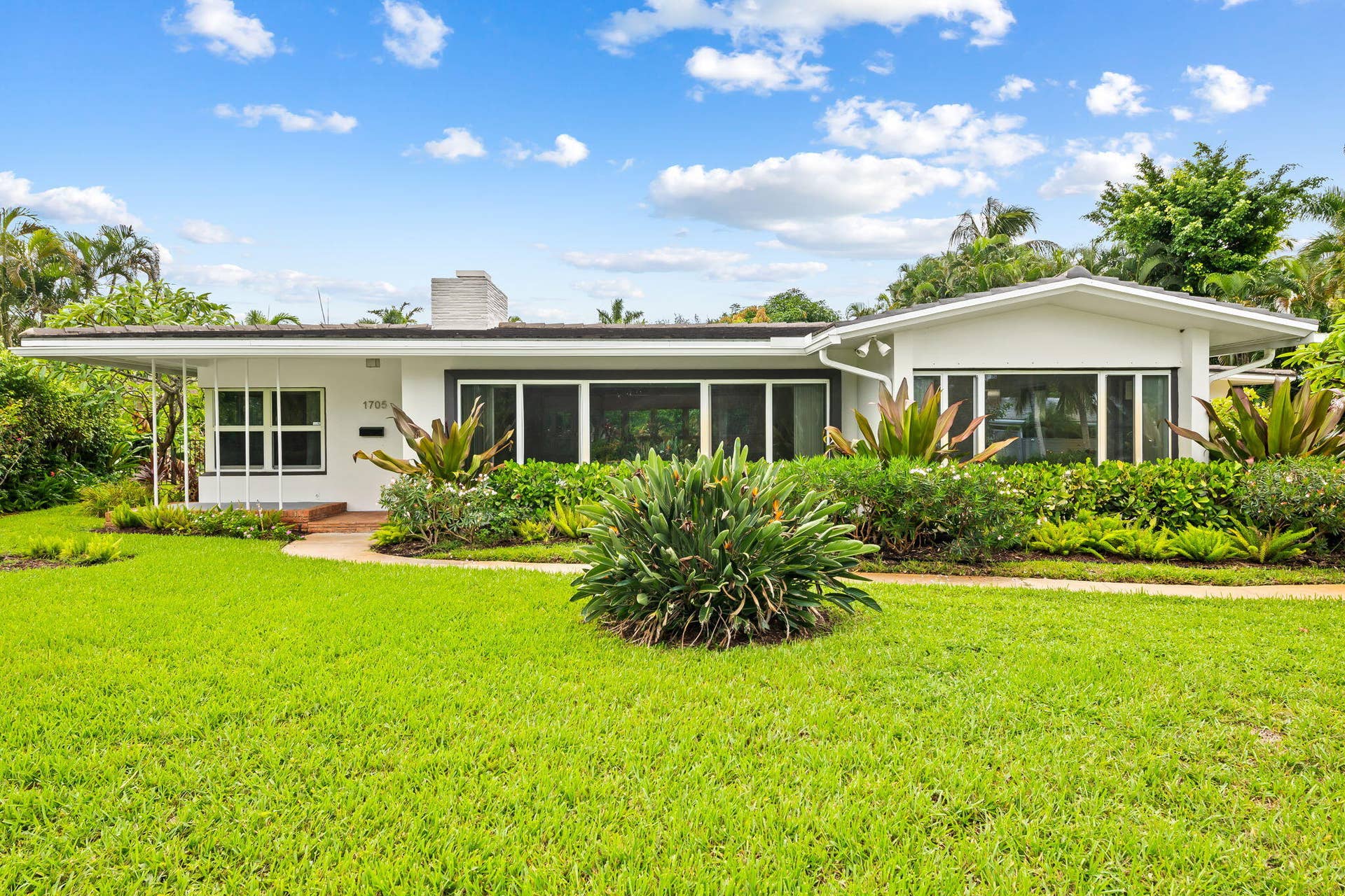 1705 NE 26TH Avenue, Fort Lauderdale, FL 33305 Ranch-style residence featuring a white exterior, expansive front lawn, lush landscaping, and a covered entryway