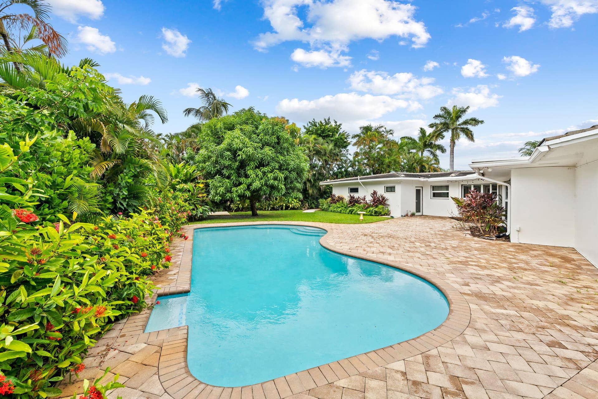 1705 NE 26TH Avenue, Fort Lauderdale, FL 33305 Freeform swimming pool with integrated steps, surrounded by a paver patio and tropical landscaping