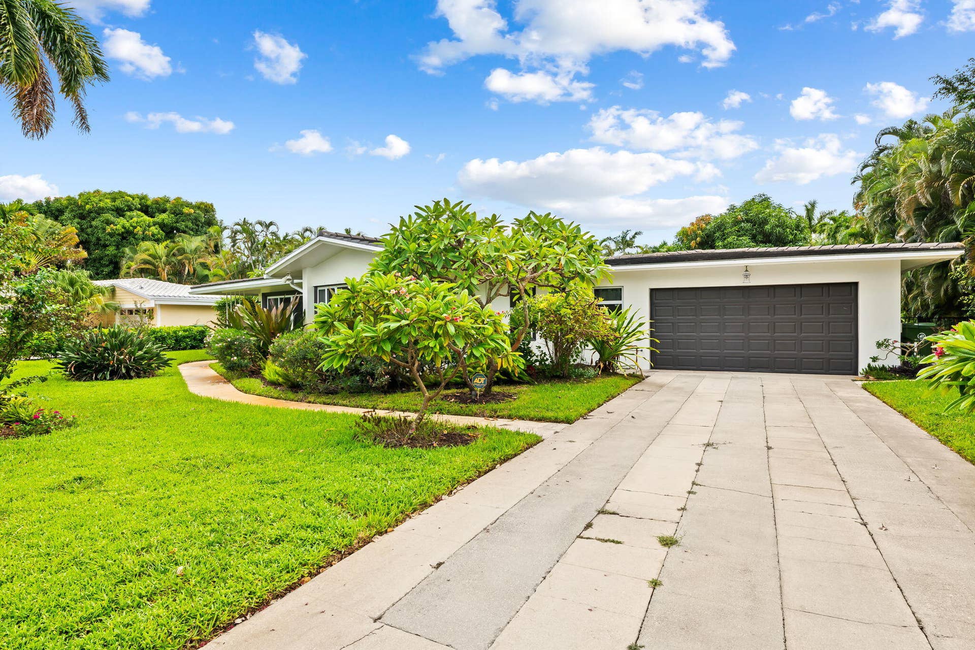 1705 NE 26TH Avenue, Fort Lauderdale, FL 33305 Expansive front yard featuring lush green lawn, mature tropical landscaping, and a curved concrete pathway