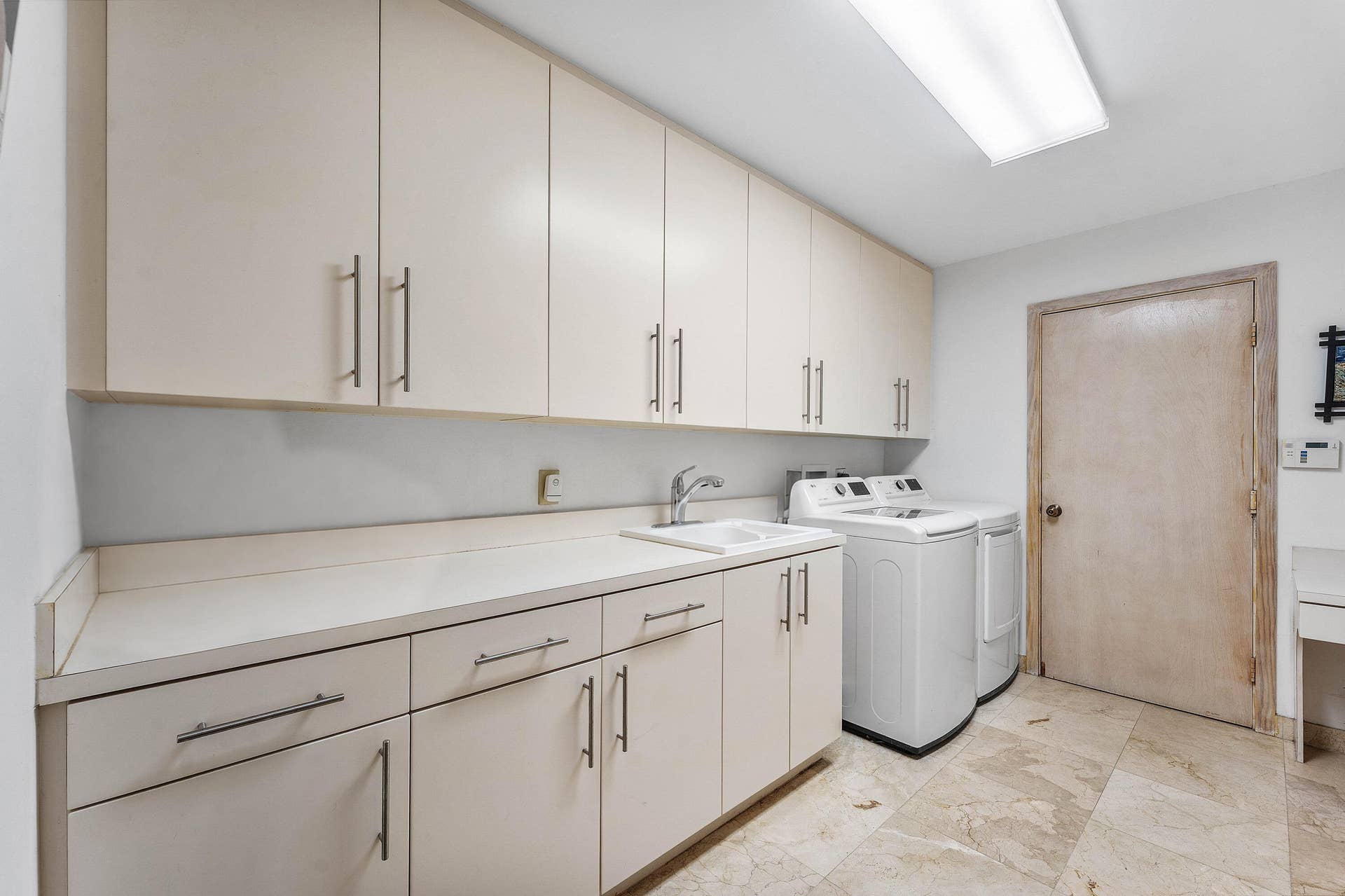 56 NORTHWOODS Lane, Boynton Beach, FL 33436 Laundry room featuring extensive upper and lower cabinetry, a built-in sink, solid surface countertops, and stone tile flooring
