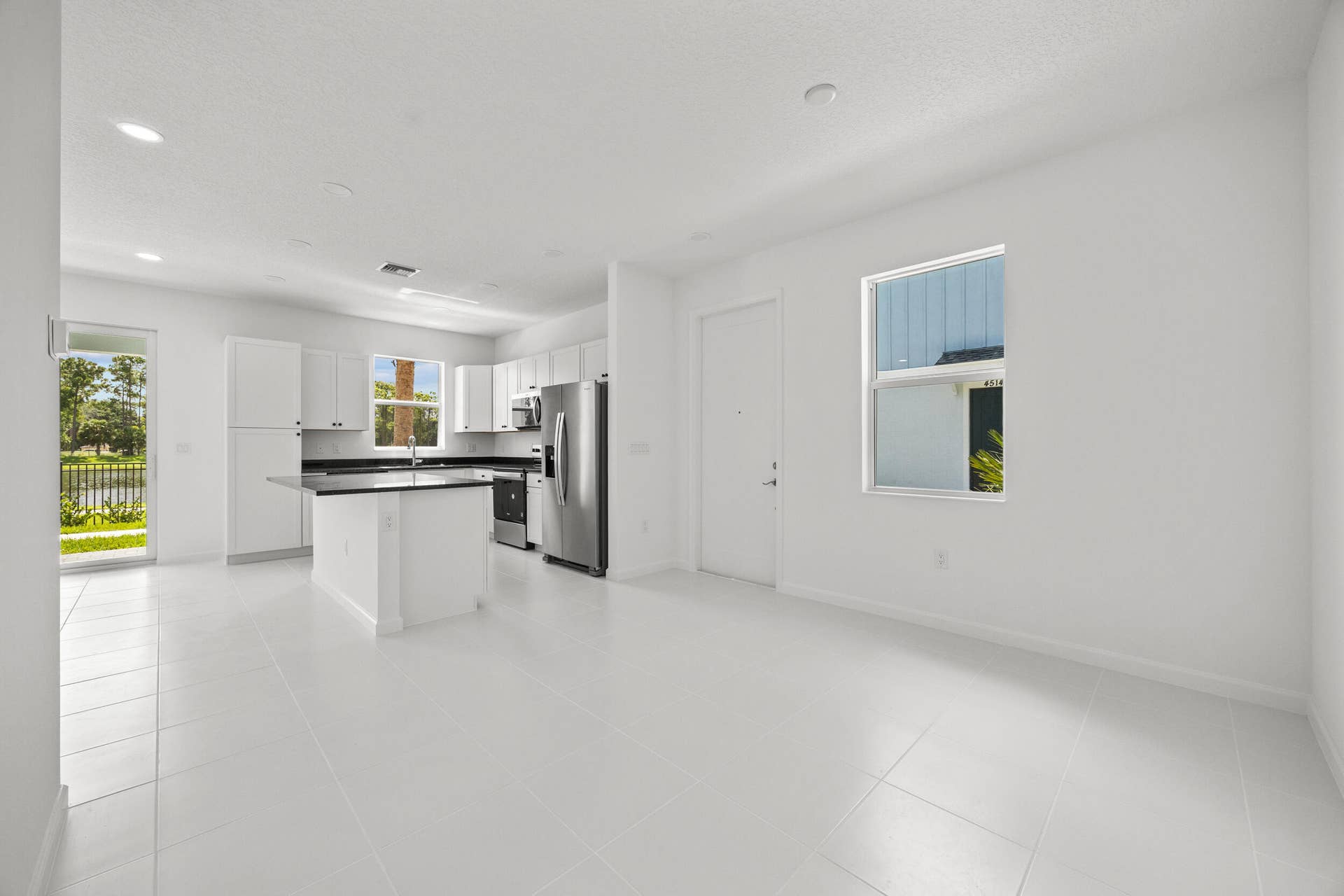 Open-concept living space featuring white tile flooring, recessed lighting, and a kitchen with white cabinetry, dark countertops, and stainless steel appliances