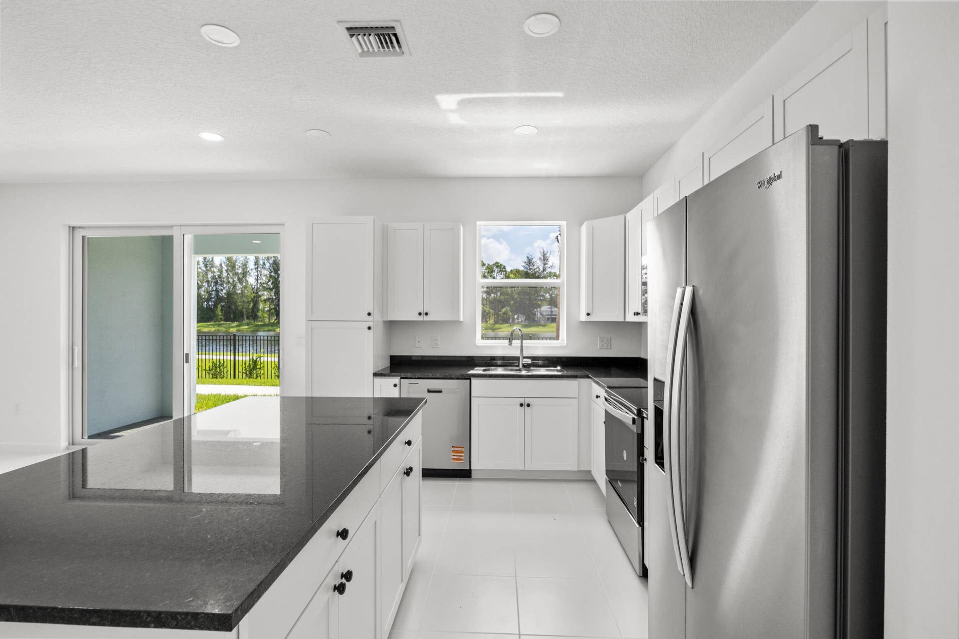 Modern kitchen featuring white cabinetry, dark countertops, stainless steel appliances, and a sliding glass door