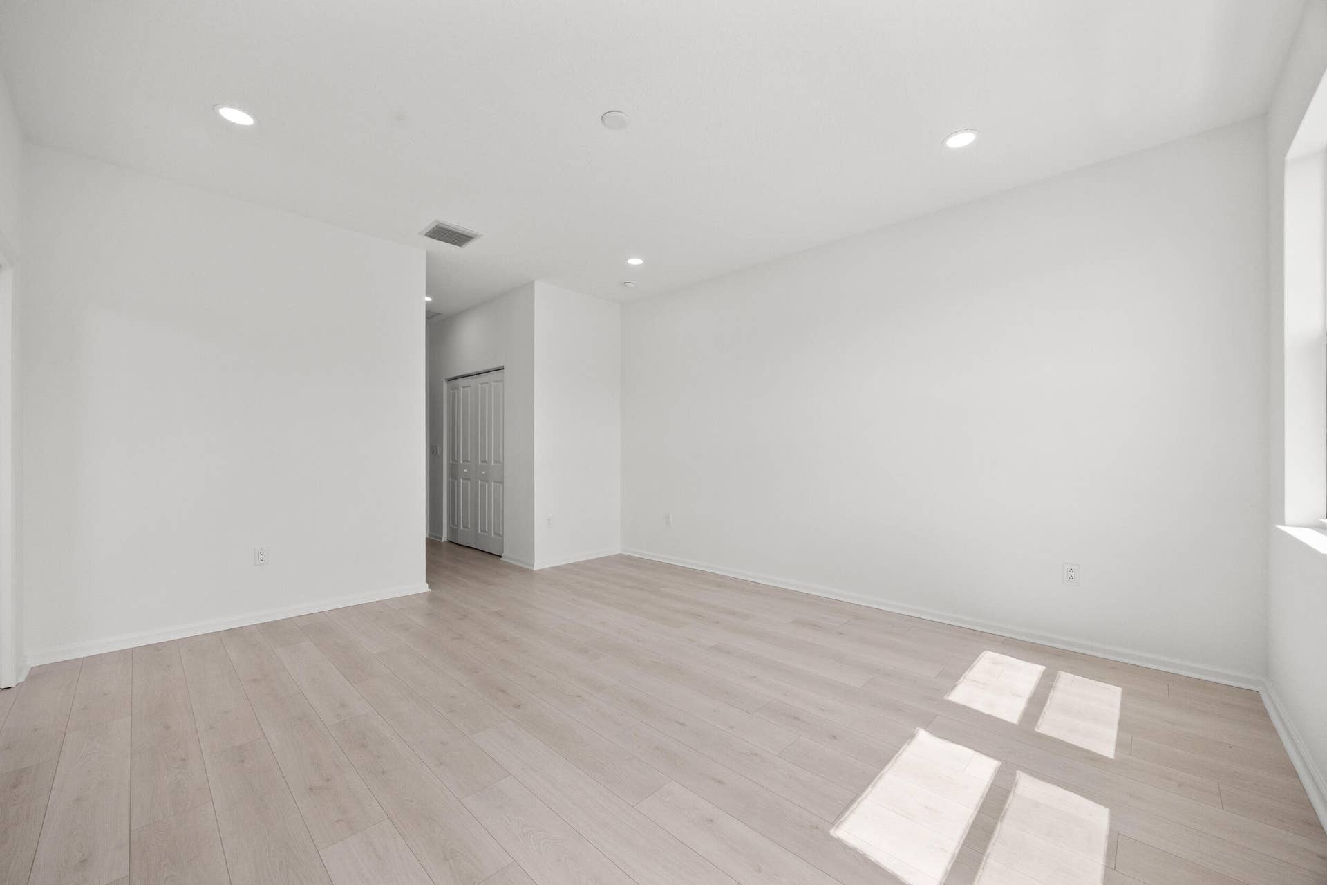 Recessed lighting throughout, wood-finish flooring, white walls, and a window for natural light