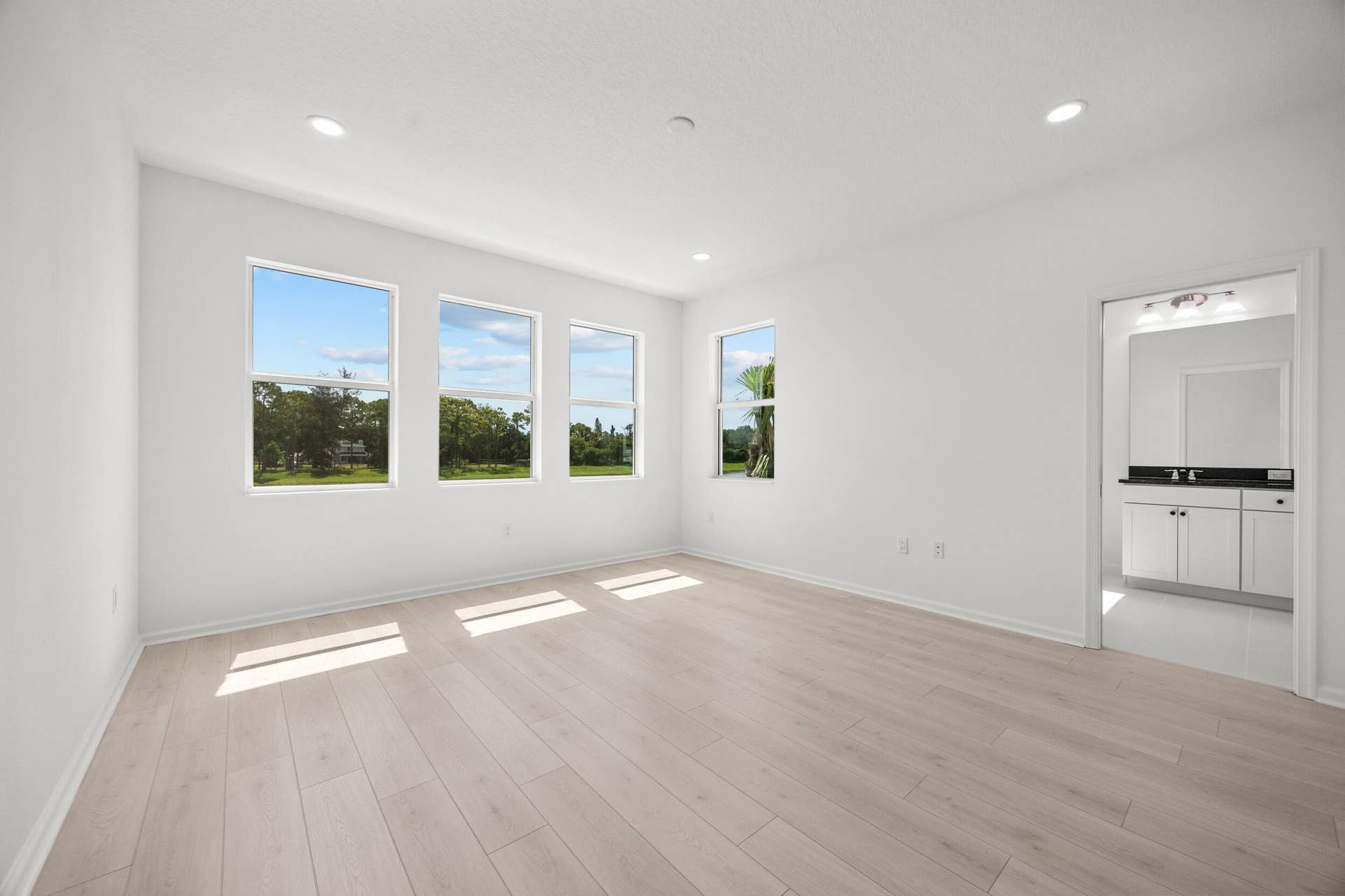 Recessed lighting, light wood-finish flooring, multiple windows, and crisp white walls