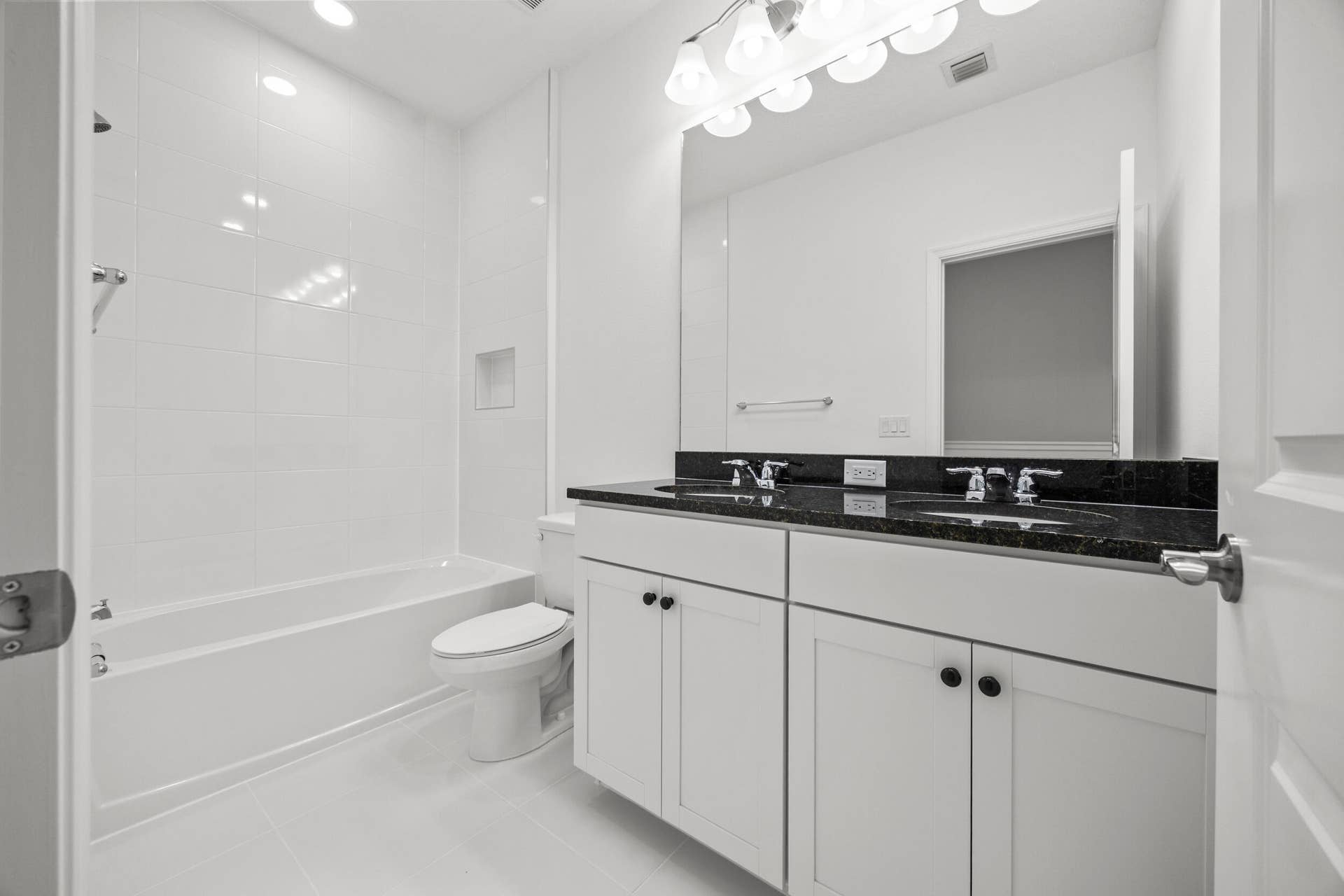Dual vanity with a dark countertop and undermount sinks, white cabinetry, integrated bathtub with a shower, and tiled walls
