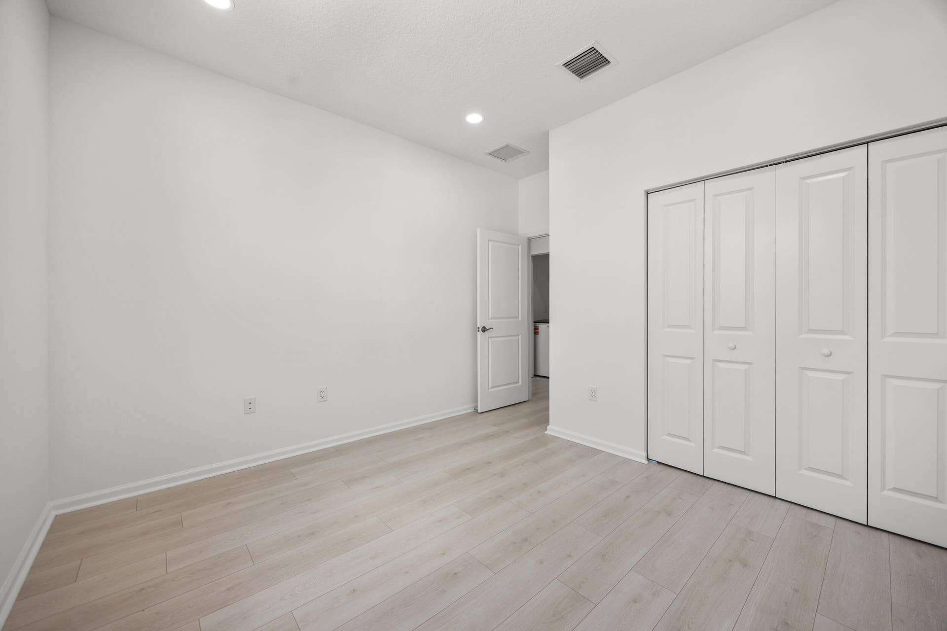 Light wood-finish flooring with white baseboards, recessed ceiling lighting, and bi-fold closet doors