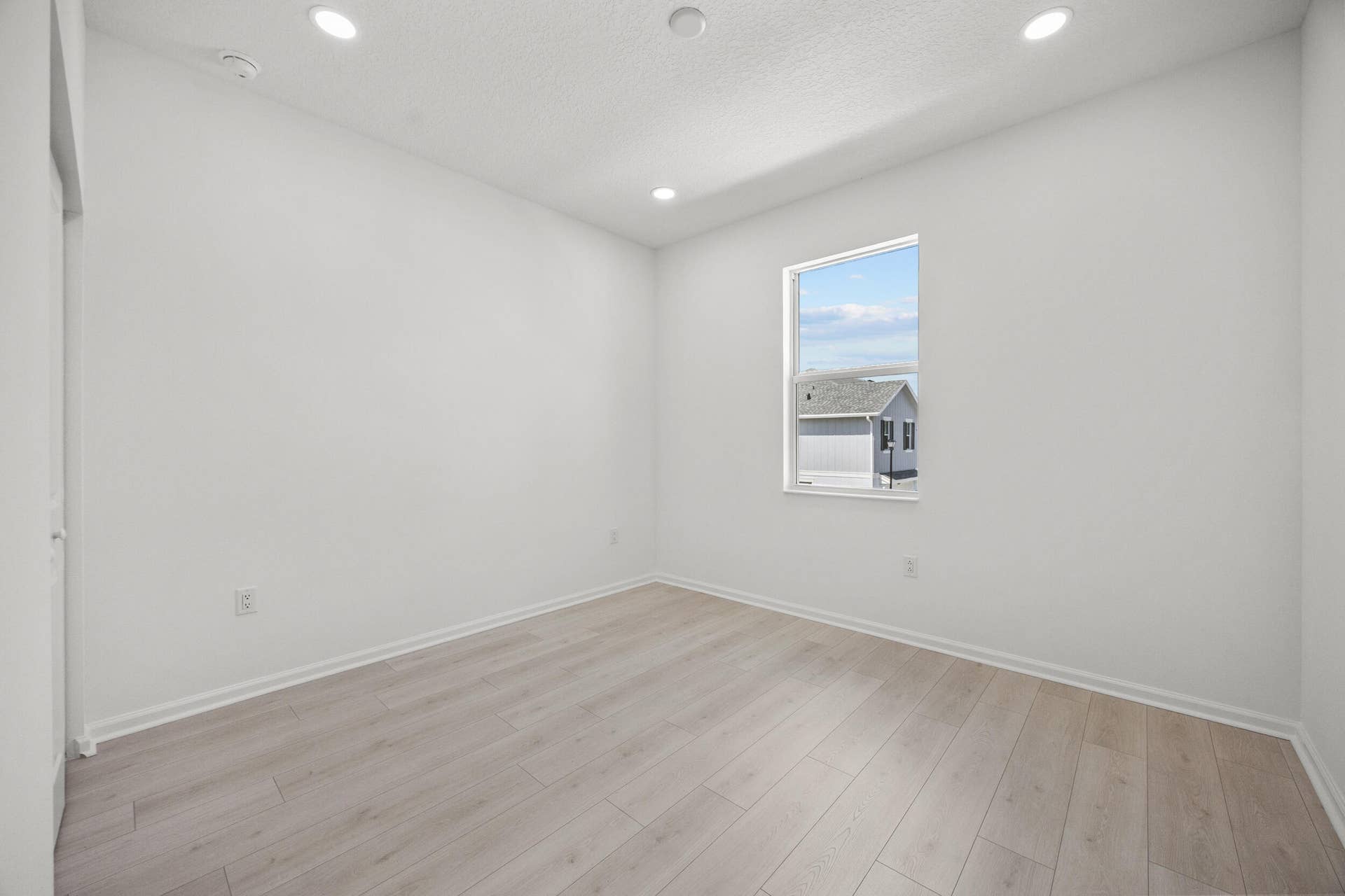 Recessed ceiling lighting, light wood-finish flooring, white walls, and a window with white trim