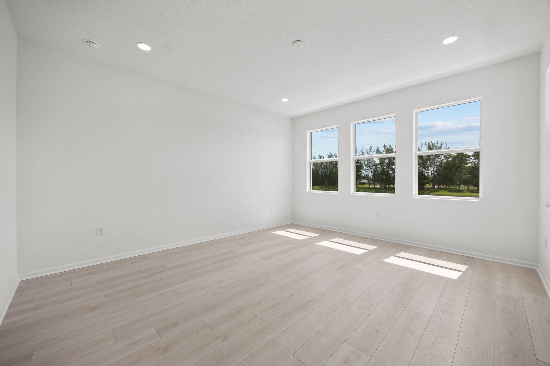 Expansive room with neutral white walls, recessed ceiling lighting, and wood-finish flooring